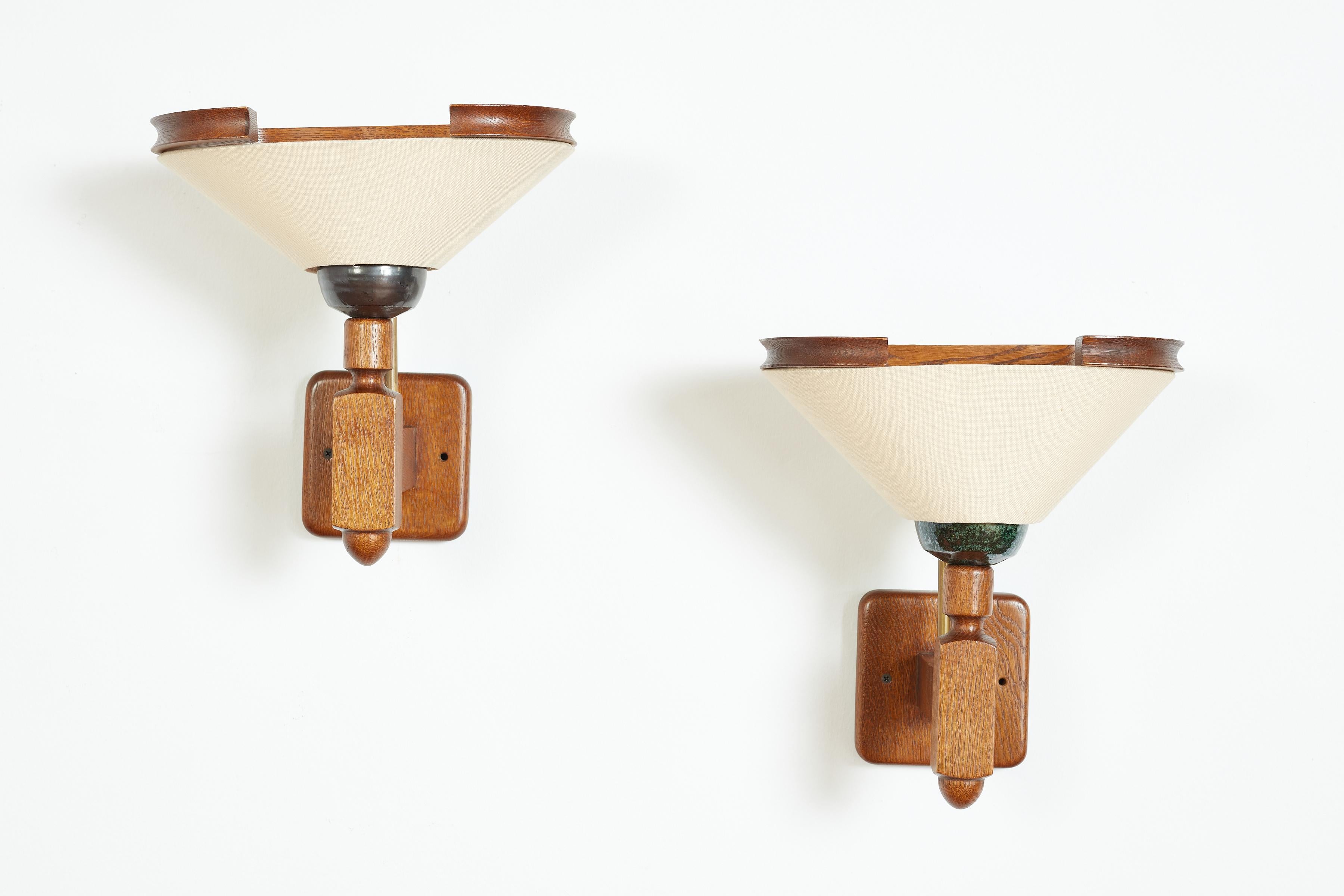 Guillerme et Chambron pair of sconces with dark ceramic sockets and new silk shades.  Oak frames with brass detailing.  
Wonderful pair. 
France circa 1940s