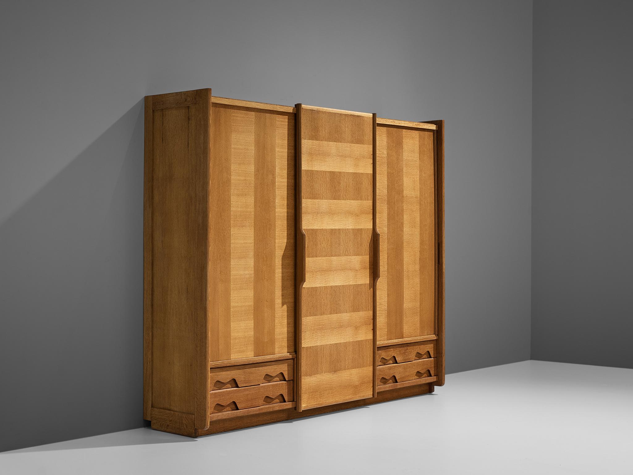 Guillerme et Chambron, wardrobe, oak, France, 1960s.

Three sliding doors structure this wardrobe designed by Guillerme et Chambron. Two doors are expanded with two bottom drawers which show decorative forms. The doors are visually structured by