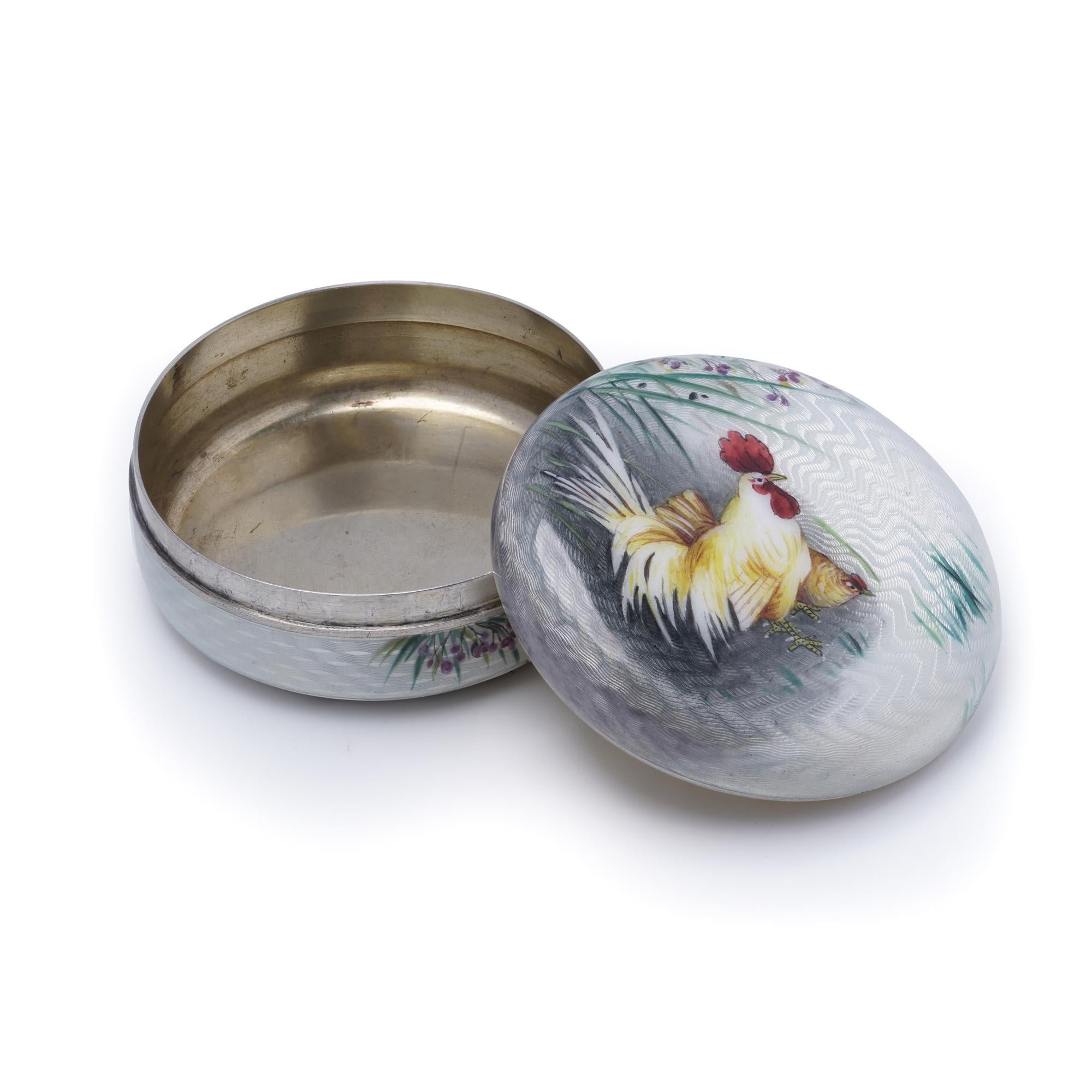 Una caja única de plata con esmalte guilloché, con un motivo de gallo finamente trabajado.
La pieza tiene un sello de plata 900.

Especificaciones:
Material: Plata, esmalte guilloché
Sellos: Plata 900
Periodo: Principios del siglo XX
Origen: Europa