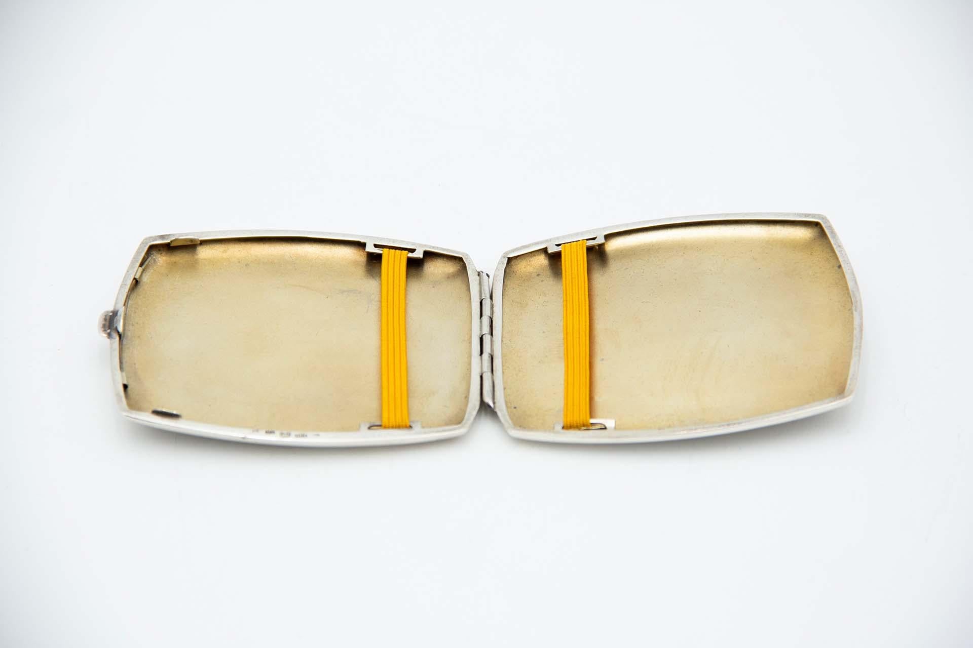 Description: Guilloche silver cigarette case with asymmetrical elements, gold interior and spring-loaded hinged lid. . Metal: Silver. Origin: German. Brand: Unknown. Weight: 86.69 grams. Dimensions: 9.2cmx1cm. Content: 900/1000. Assay Mark: Yes.