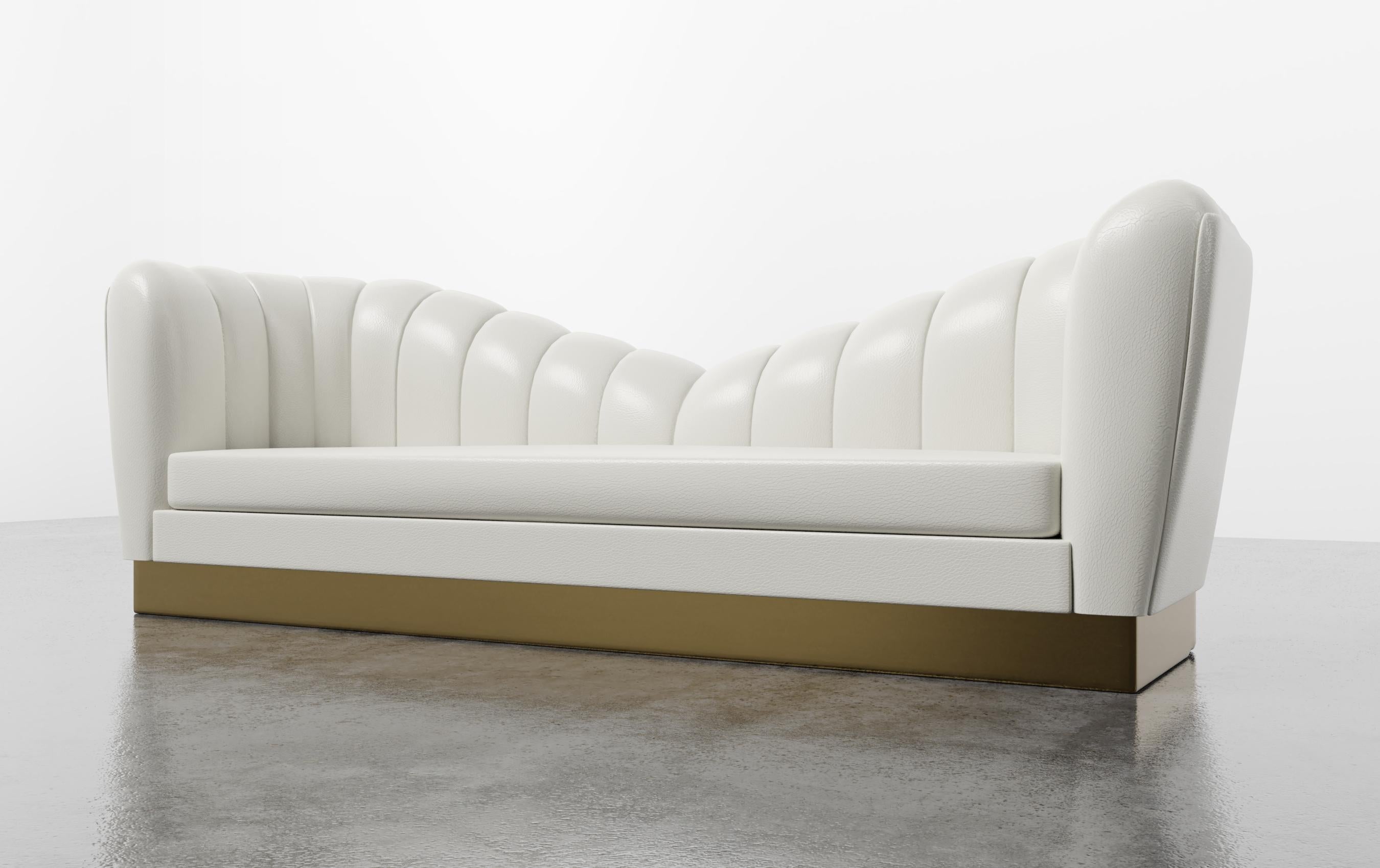 GUINEVERE SOFA - Modern Symmetrical Sofa in Faux White Leather with Metal Plinth

The Guinevere Sofa is a luxurious piece of furniture that takes inspiration from the curvature of Gaudi architecture. It features symmetrical channeled scalloped