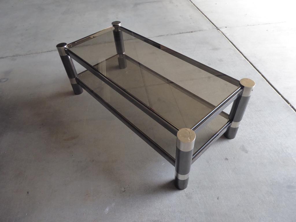 A gunmetal and nickel-plated two-tier coffee table made by American design icon Karl Springer in the 1970s. Each shelf has the original smoked glass. There is an impressed signature present on one side of the lower level. The plating has been