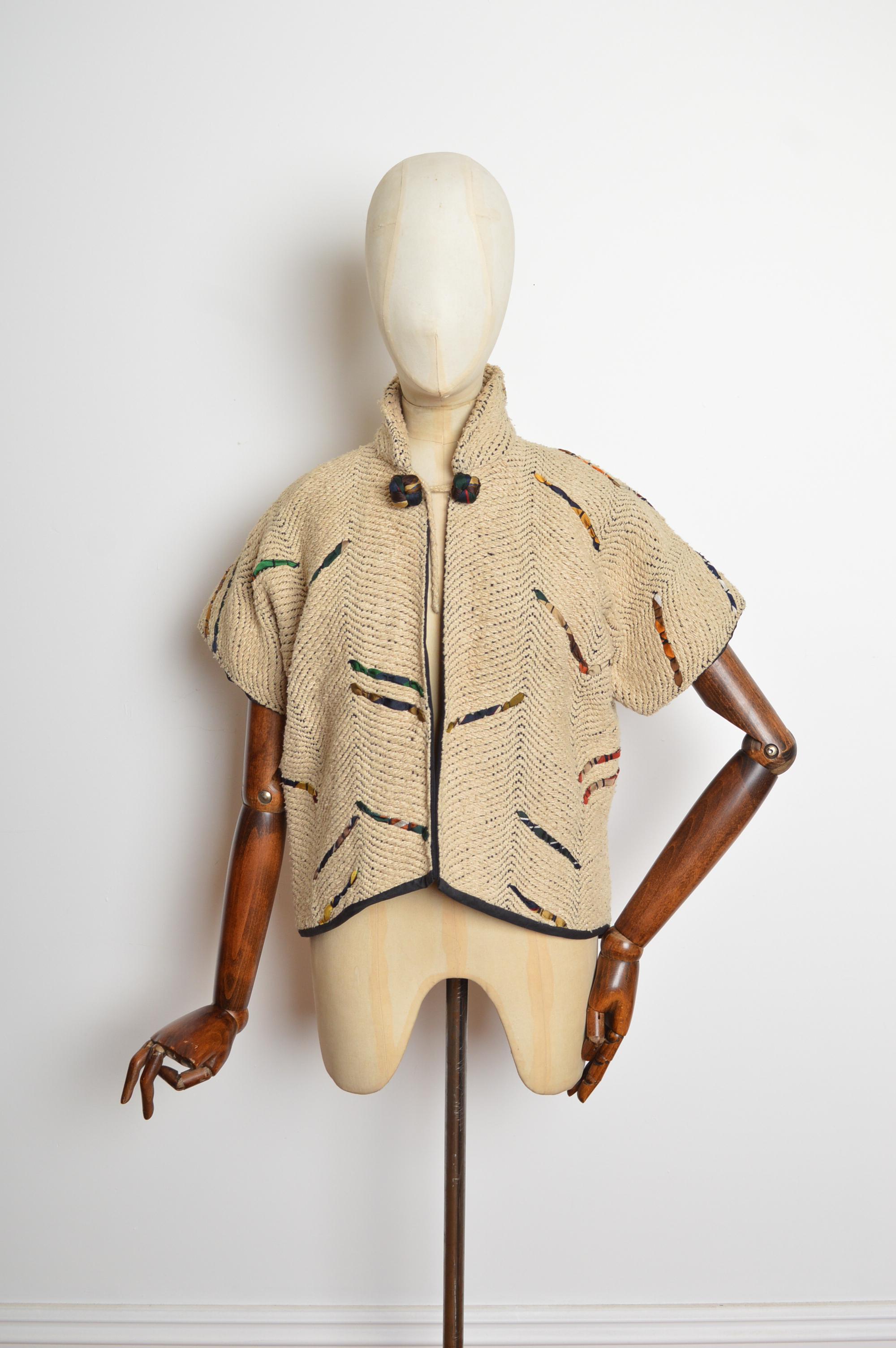 Une fabuleuse veste d'avant-garde ajustée à manches courtes de GUN Trigère de Hille.
Elle présente un col à fermeture par nœuds, des manches courtes et une silhouette ajustée au corps. Le tissu est un épais tissage beige avec un ruban de soie