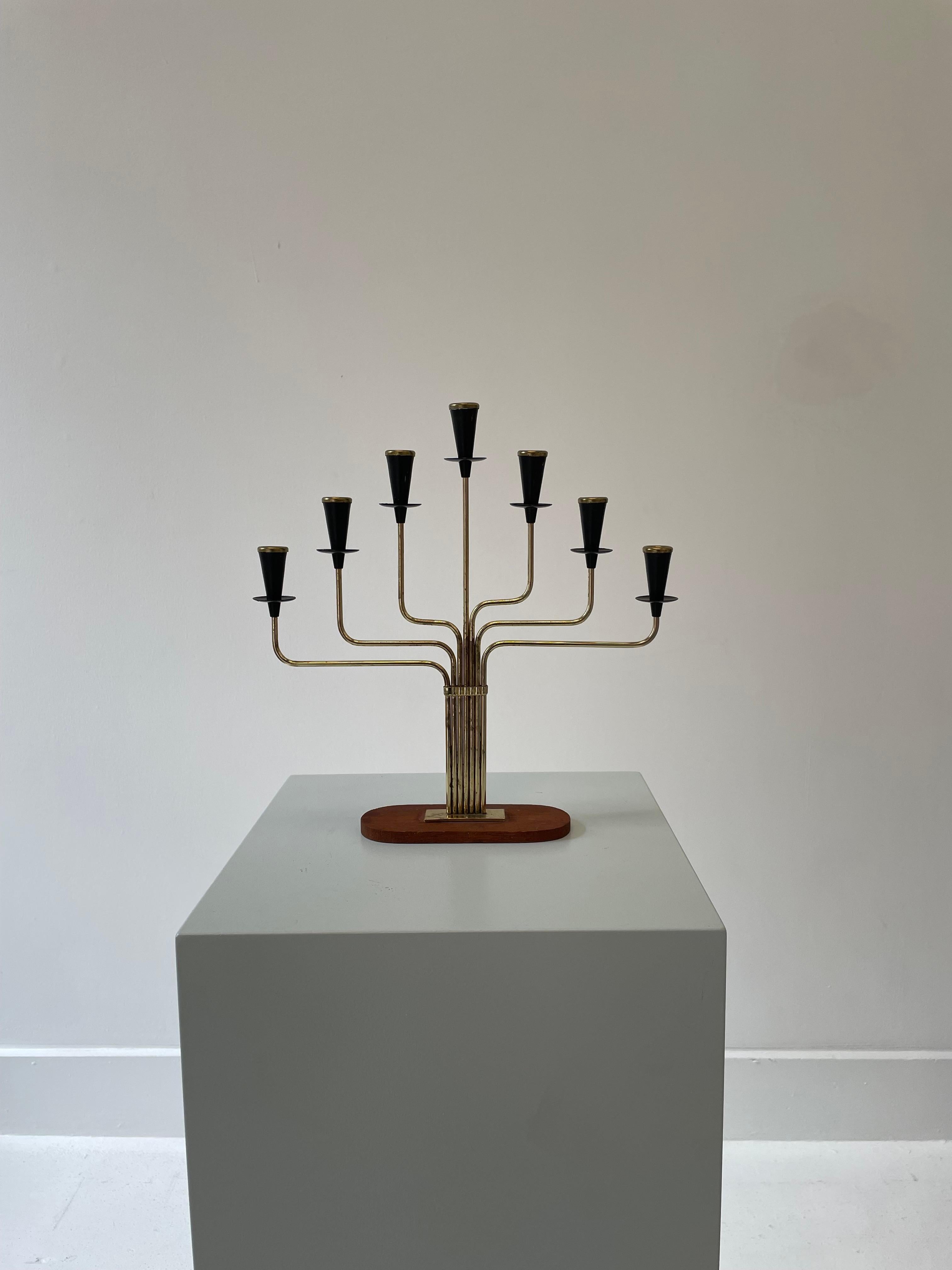 Height: 27cm
Width: 29cm
Depth: 6cm

Designer: Gunnar Ander 
Date: 1950s
Materials: Teak, brass, patinated brass

Description: Six candleholders flay the central post in this design. The brass has even patination across the surface.
