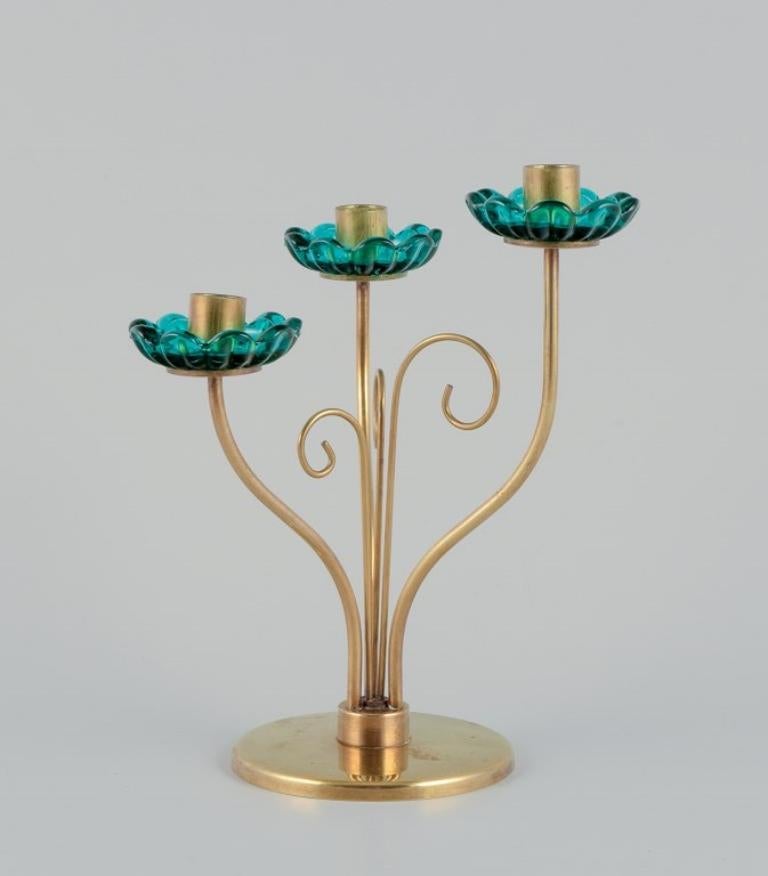 Gunnar Ander for Ystad Metall, Sweden. 
Brass candlestick holder with turquoise glass sleeves. For three candles.
Circa 1960.
Perfect condition.
Suitable for candles with a diameter of 12 mm.
Dimensions: H 16.5 cm x D 13.0 cm.