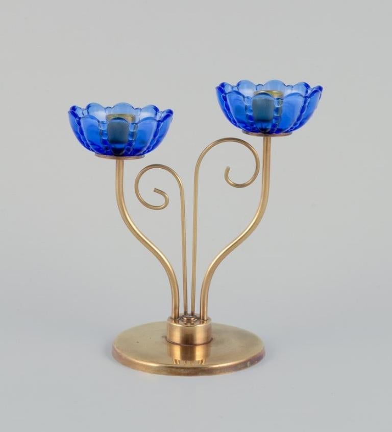 Gunnar Ander for Ystad Metall, Sweden. 
Brass candlestick holder with blue glass sleeves. For two candles.
Circa 1960.
Perfect condition.
Suitable for candles with a diameter of 12 mm.
Dimensions: H 13.6 cm x W 12.3 cm.