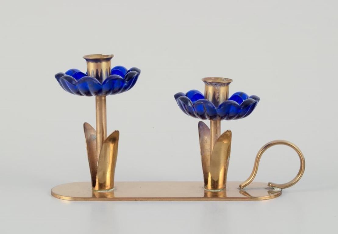 Gunnar Ander for Ystad Metall, Sweden. 
Candlestick holder in brass and blue art glass shaped like flowers. For two candles.
From the 1950s.
In excellent condition with good patina.
Dimensions: W 13.5 cm x H 8.0 cm.