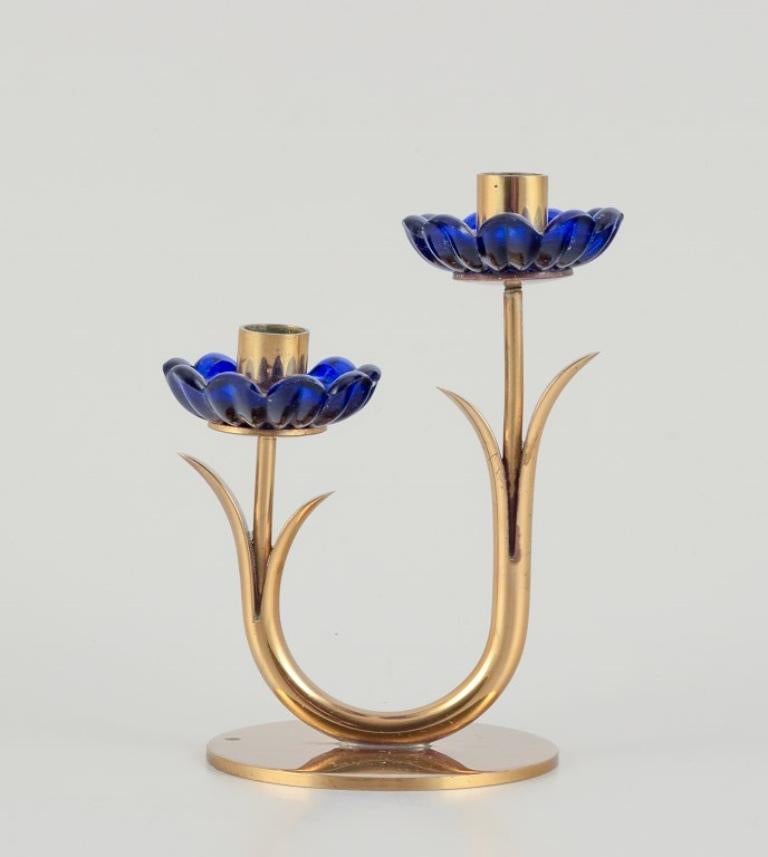 Gunnar Ander for Ystad Metall, Sweden. 
Candlestick holder in brass and blue art glass shaped like flowers. 
For two candles.
From the 1950s.
In excellent condition with good patina.
Marked.
Dimensions: W 9.5 cm x H 12.5 cm.