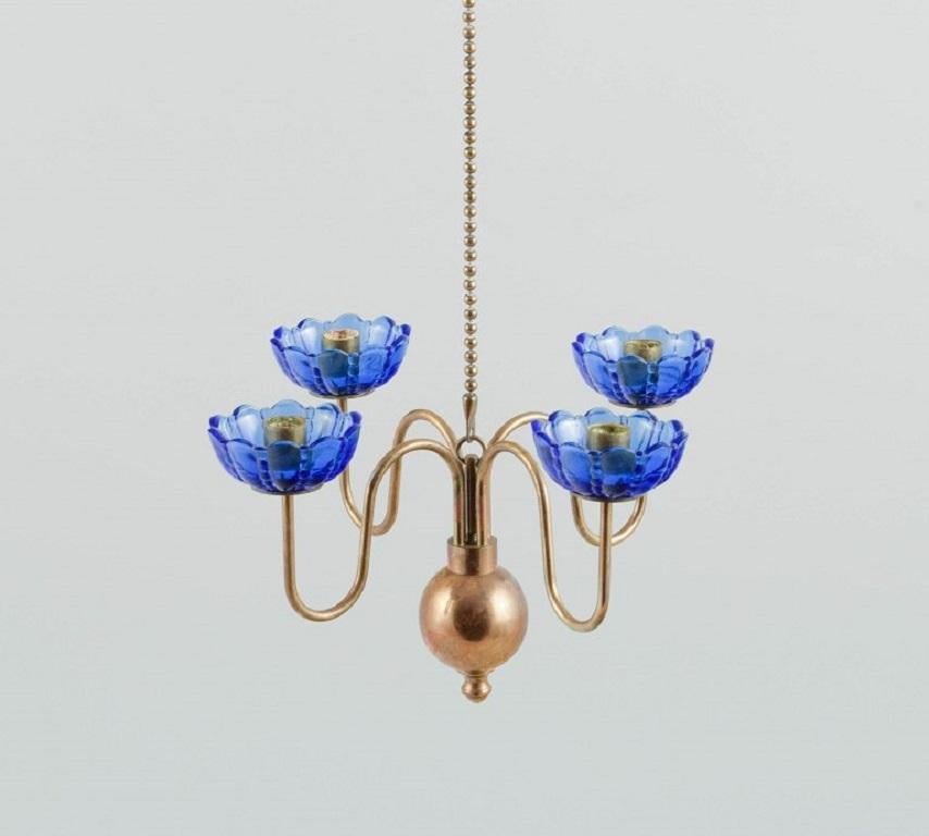 Gunnar Ander for Ystad Metall. 
Chandelier for four candles in brass and mouth-blown art glass shaped like flowers. Scandinavian design, mid-20th century.
Measures: 21 x 12.5 cm.
Chain length: 72 cm.
In excellent condition.

