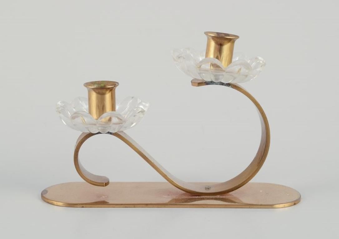Gunnar Ander for Ystad Metall, Sweden. 
Candlestick holder in brass and clear art glass shaped like flowers. 
For two candles.
From the 1950s.
In excellent condition with good patina.
Dimensions: W 12.0 cm x H 7.7 cm.