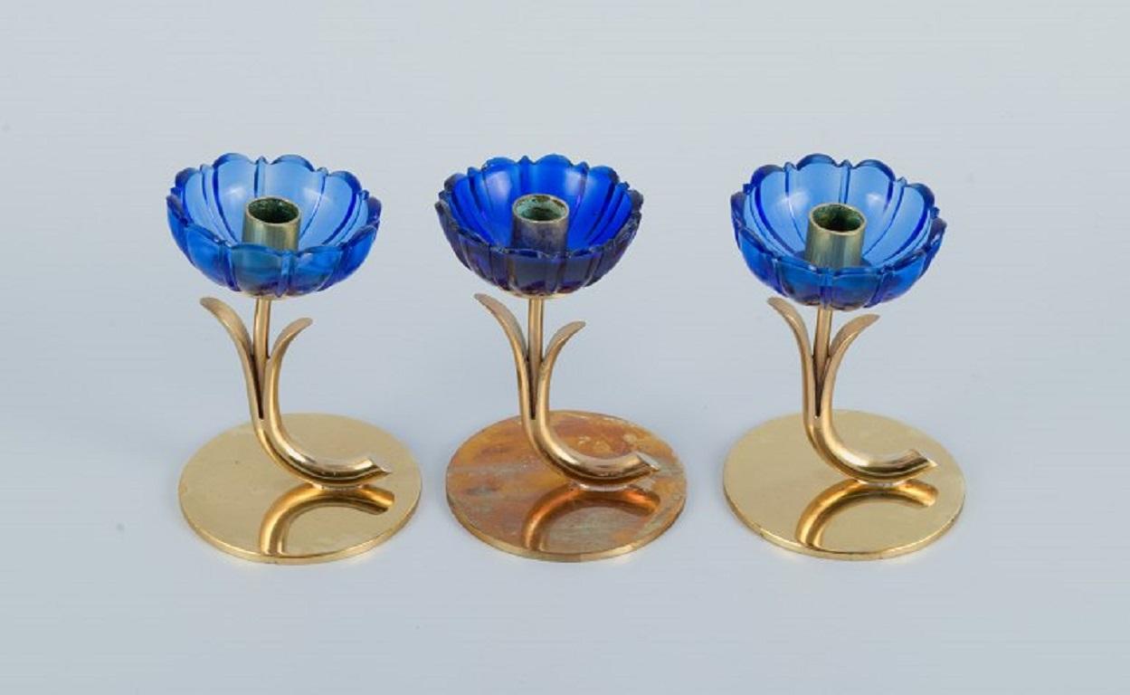 Gunnar Ander for Ystad Metall. 
Three candlesticks in brass and blue art glass shaped like flowers.
1950s.
Measurements: H 9.0 cm. x W 6.0 cm.?
Fits candles with a diameter of 10 mm.
In excellent condition.