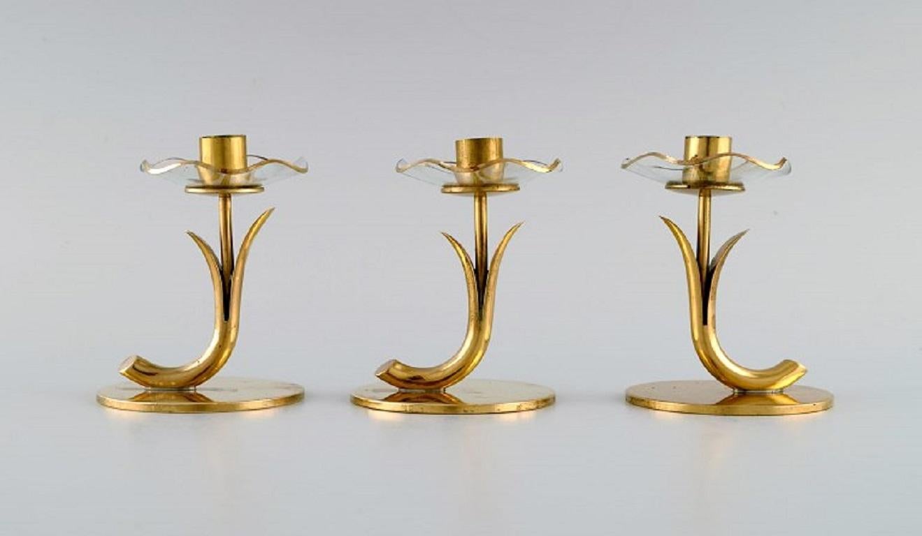 Gunnar Ander for Ystad Metall. Three candlesticks in brass and clear art glass shaped like flowers. 1950s.
Measures: 8.5 x 6.5 cm. 
In excellent condition.
Stamped.