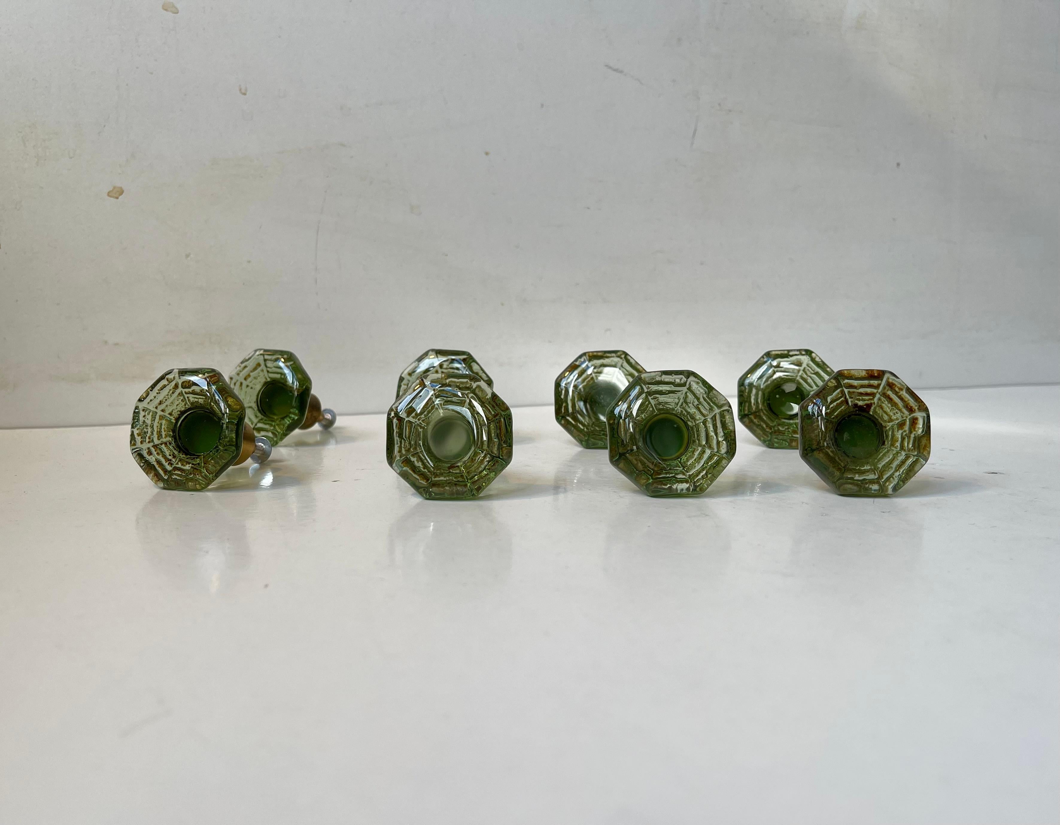 A rare set of 8 olive green glass and brass door/drawer knobs with decorative and unusual spiderweb. Designed by Gunnar Andersen for Lindshammar Glasbruk in Sweden during the 1960s.   

Measurements: Dept: 6 cm, W/H: 4 cm.  

The price is for the