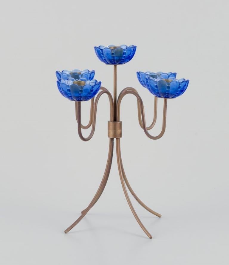 Gunnar Ander for Ystad Metall, Sweden. 
Tall candlestick holder in brass and blue art glass shaped like flowers. 
For five candles.
From the 1950s.
In excellent condition with patina.
Dimensions: D 21,0 cm. x H 22,5 cm.
