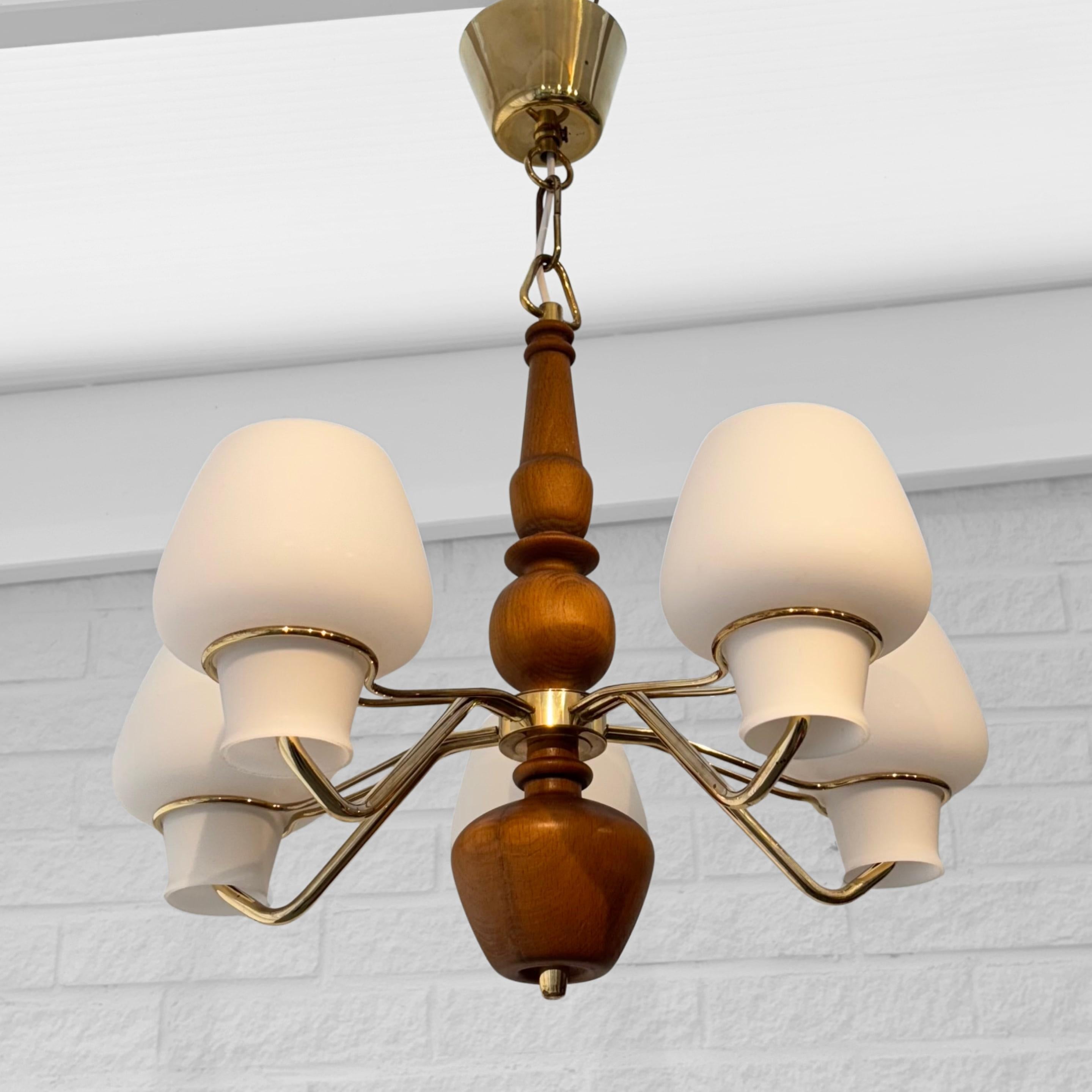 A stunning vintage chandelier designed by architect Gunnar Asplund and produced by the renowned Swedish lighting manufacturer ASEA Belysning in the 1950s. This elegant piece features a brass frame with five gracefully curved arms, each holding a