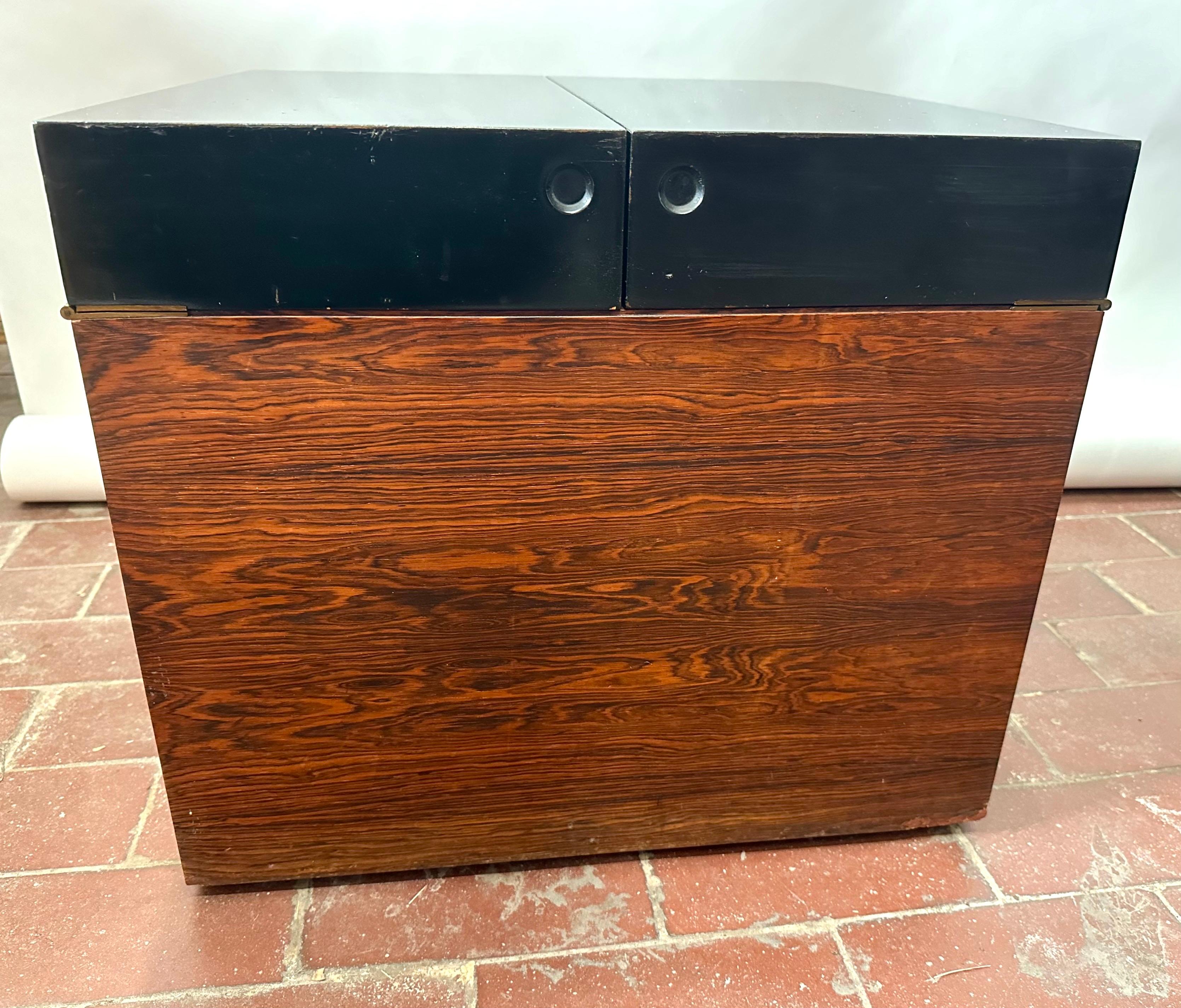 This chic bar cabinet is veneered in richly grained rosewood on the bottom case, while the hinged lid is lacquered black. When open, the lid functions as a serving surface. Inset casters allow it to easily wheel around. 

The interior is