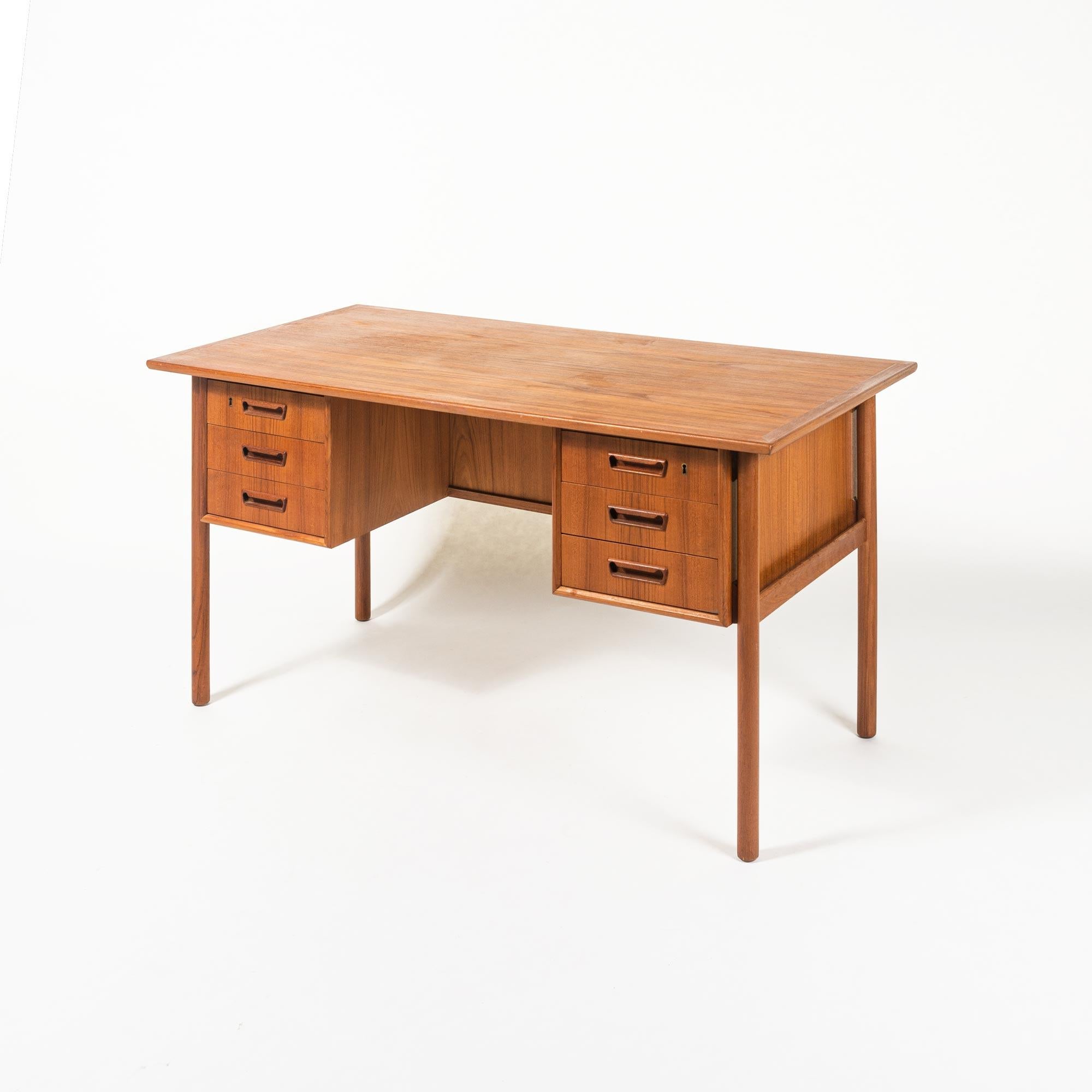This executive desk designed by G. Nielsen Tibergaard was produced in Denmark in the 1960s. The desk is made of teak and free standing thanks to the finished back side with open storage space books . On the front there are two drawer modules with