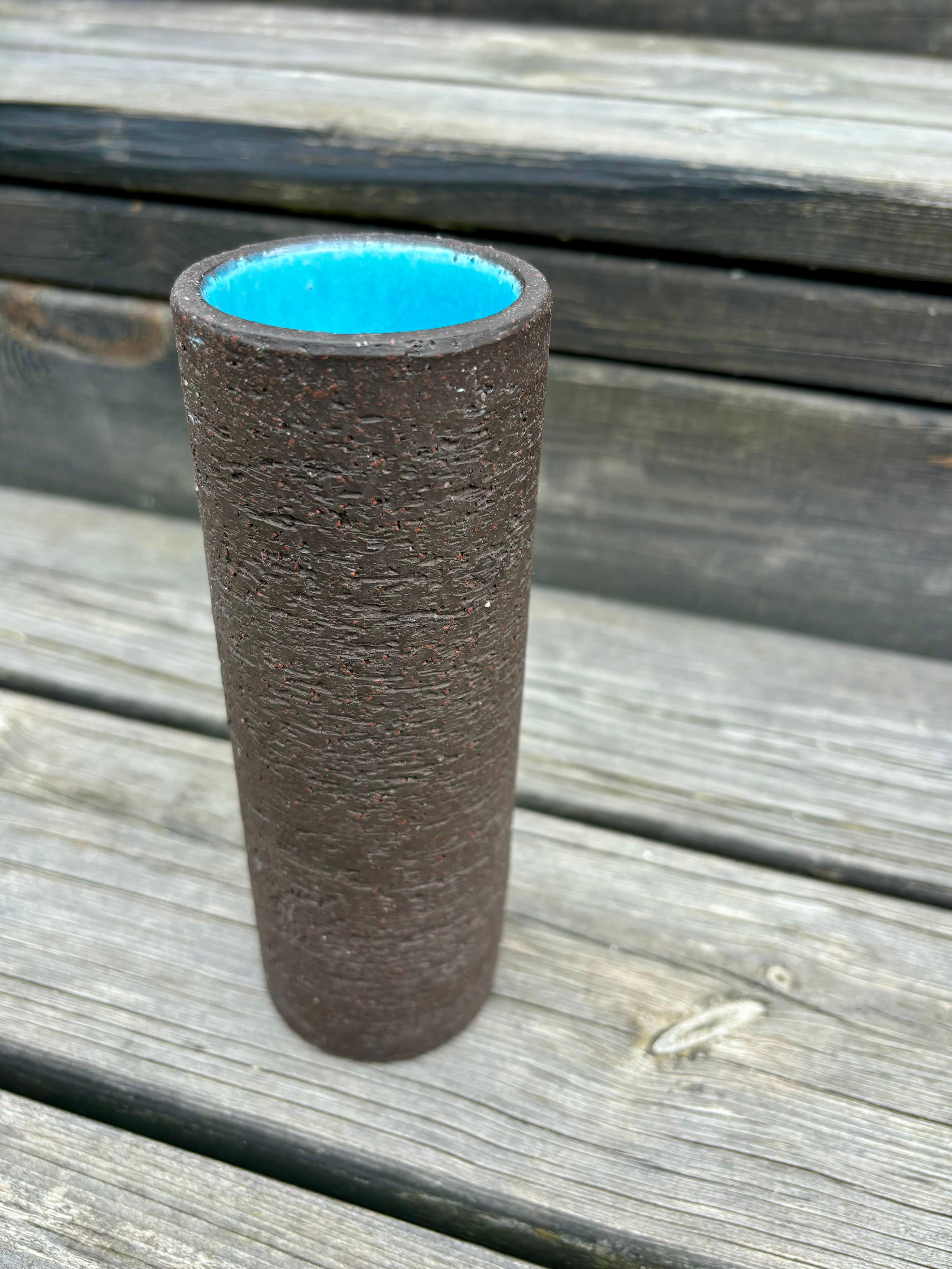 Vaso a cilindro minimalista e moderno scandinavo realizzato a mano dall'artista svedese Gunnar Nylund per Nymølle negli anni '60. Argilla chamotte rustica e opaca di colore marrone scuro all'esterno e smalto blu brillante all'interno. 
Model 5666.