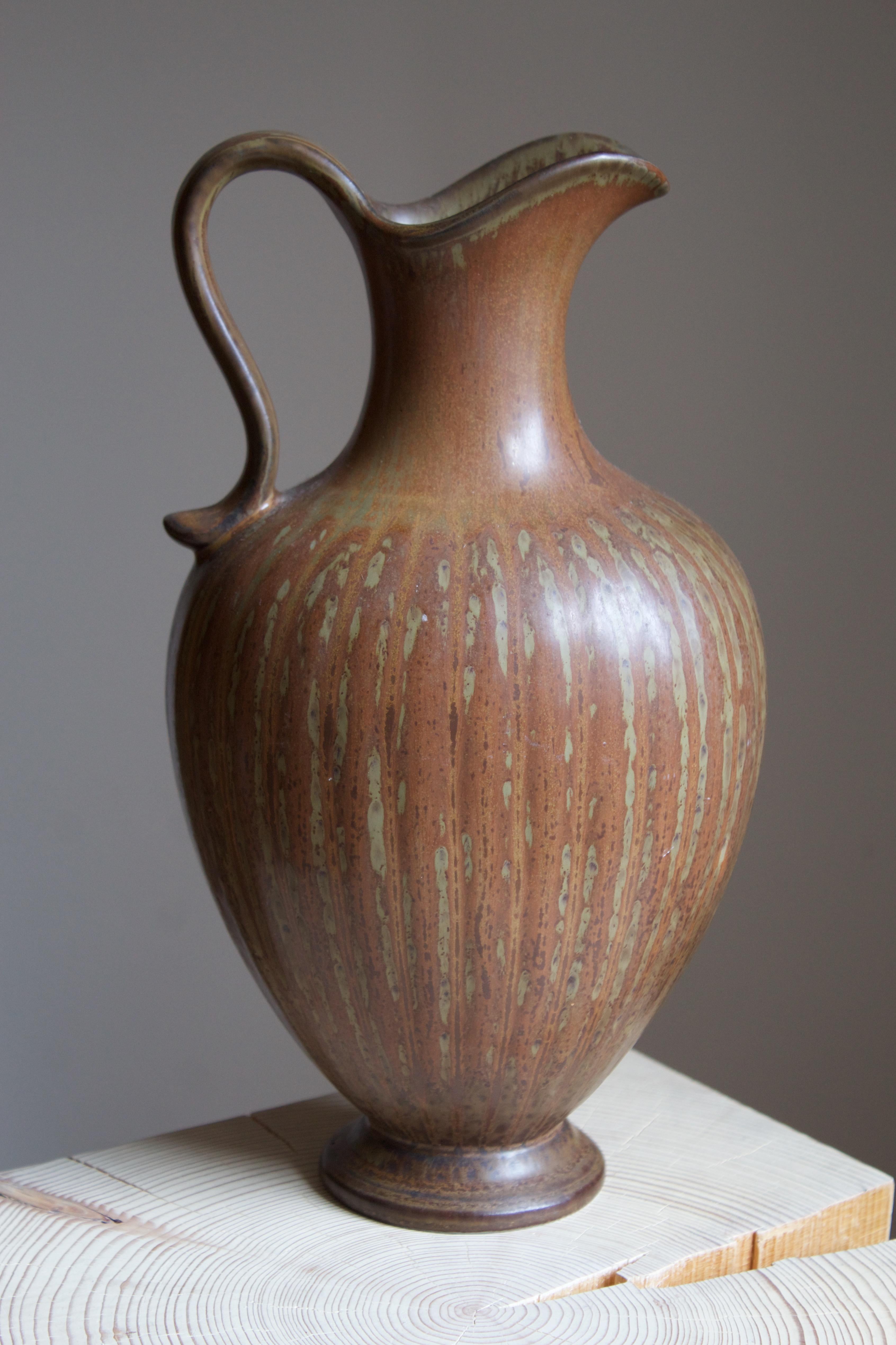 A sizable stoneware pitcher produced by Rörstrands, Sweden, 1940s. Designed and signed by Gunnar Nylund, (Swedish, 1914-1997).

Nylund served as artistic director at Rörstrands, where he worked 1931-1955. Prior to his work at Rörstrand he was a