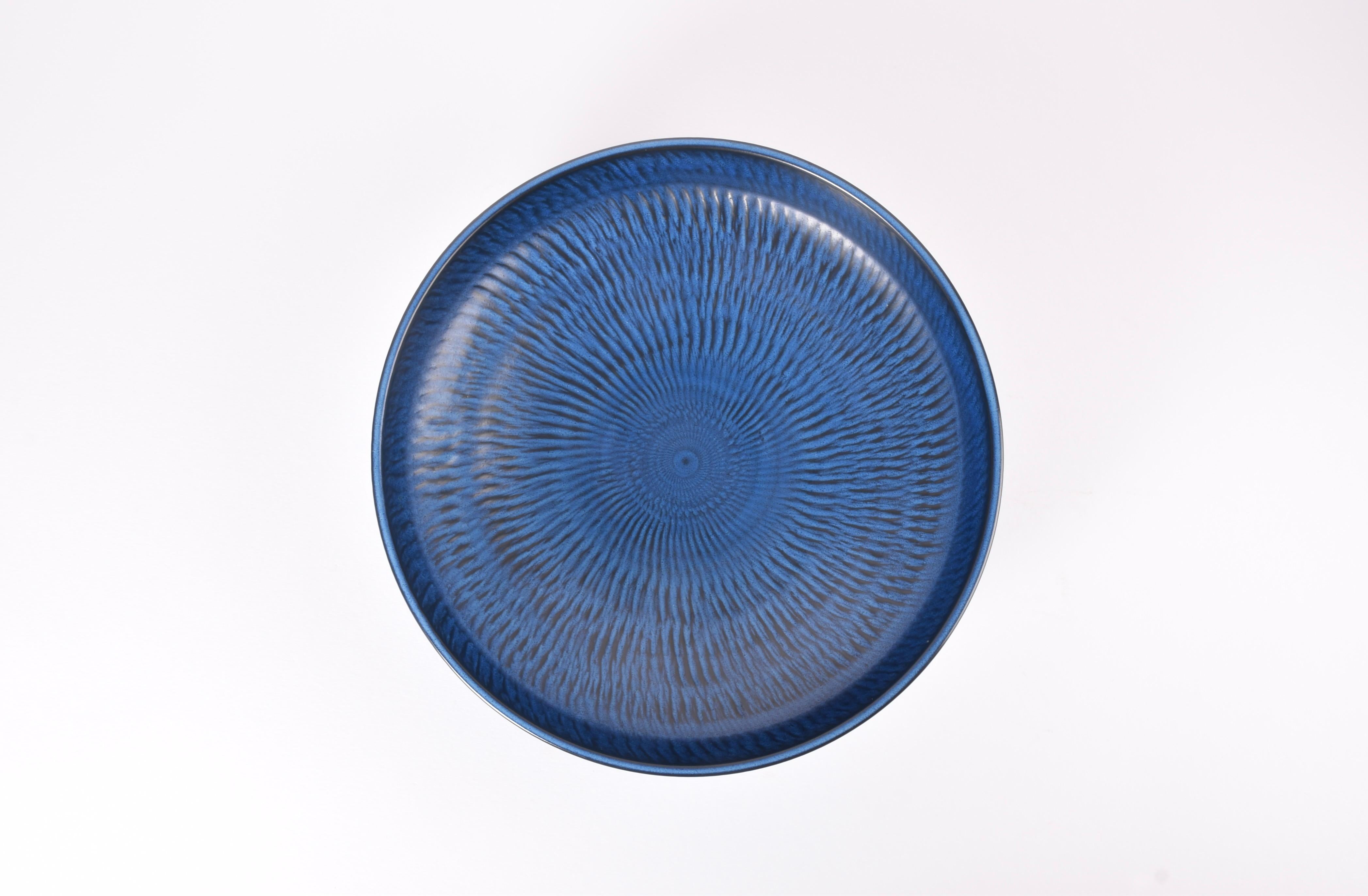 This very large circular bowl was designed by Gunnar Nylund for Nymølle and produced in Denmark, circa 1960s. It has a vivid dark blue glaze over a radiating pattern.

It would look great as a very large fruit bowl.

The bowl is a factory first