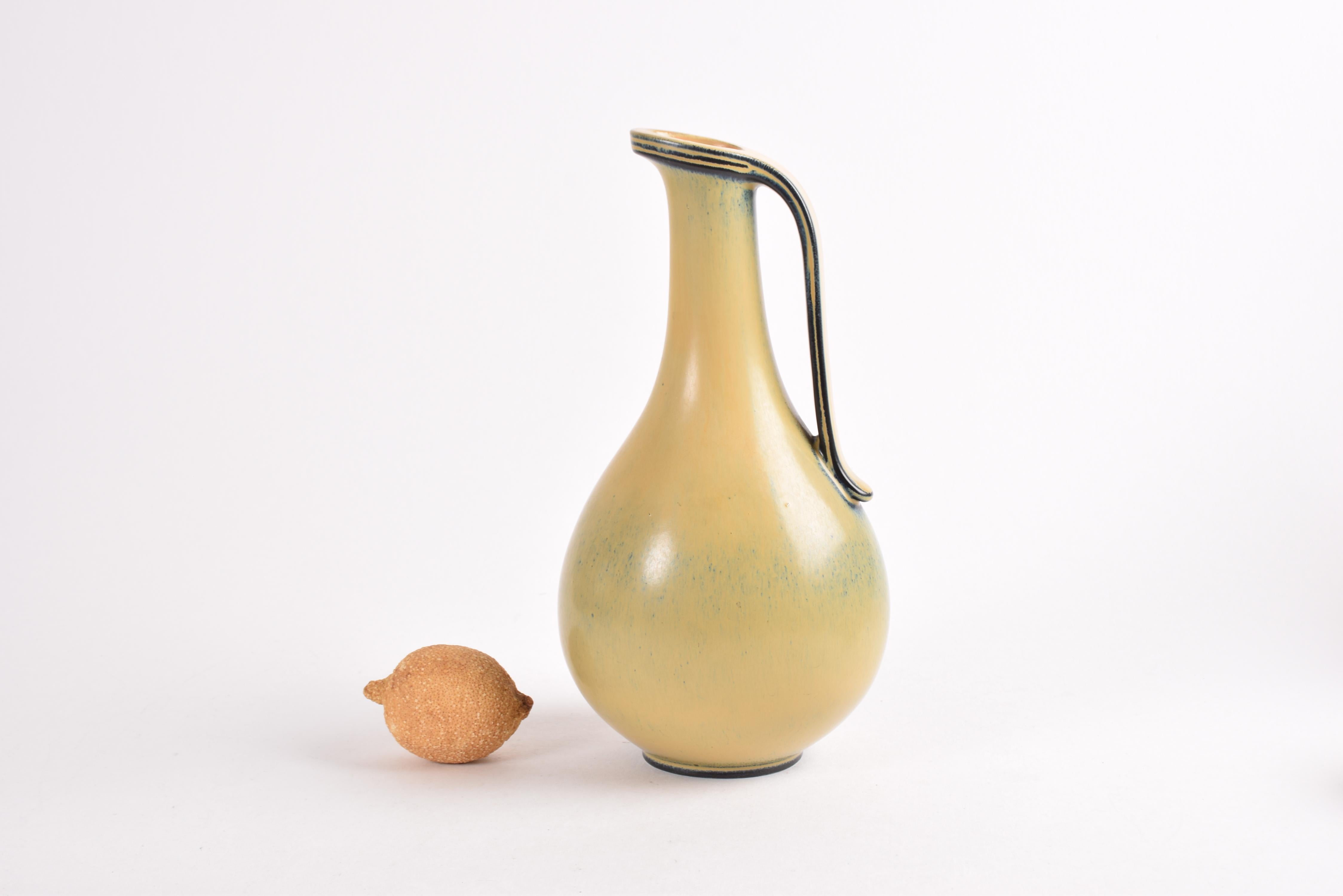 An elegant handled vase by Swedish designer Gunnar Nylund (1904-97) for Rörstrand, Sweden. Made ca 1940s to 50s.

The vase is made from stoneware and it comes in a rare version with yellow glaze with blue elements. The curves are accentuated by