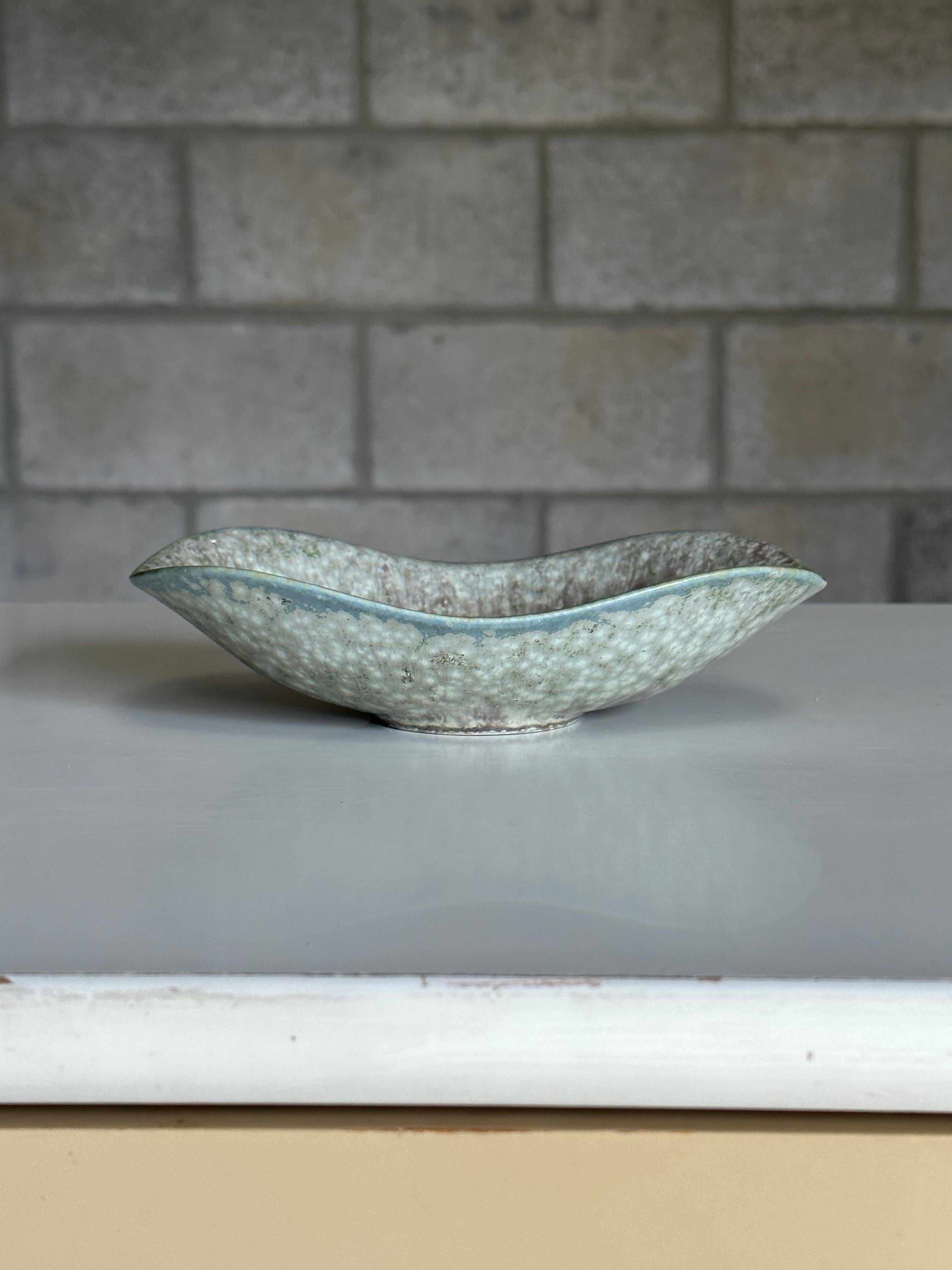 A low and small bowl or vide poche designed by Gunnar Nylund for Rörstrand. Features a light blue color with some faint yellow and green mixed in. Would make for a wonderful Vide Poche. Exceptional movement with the changing height of the rim
