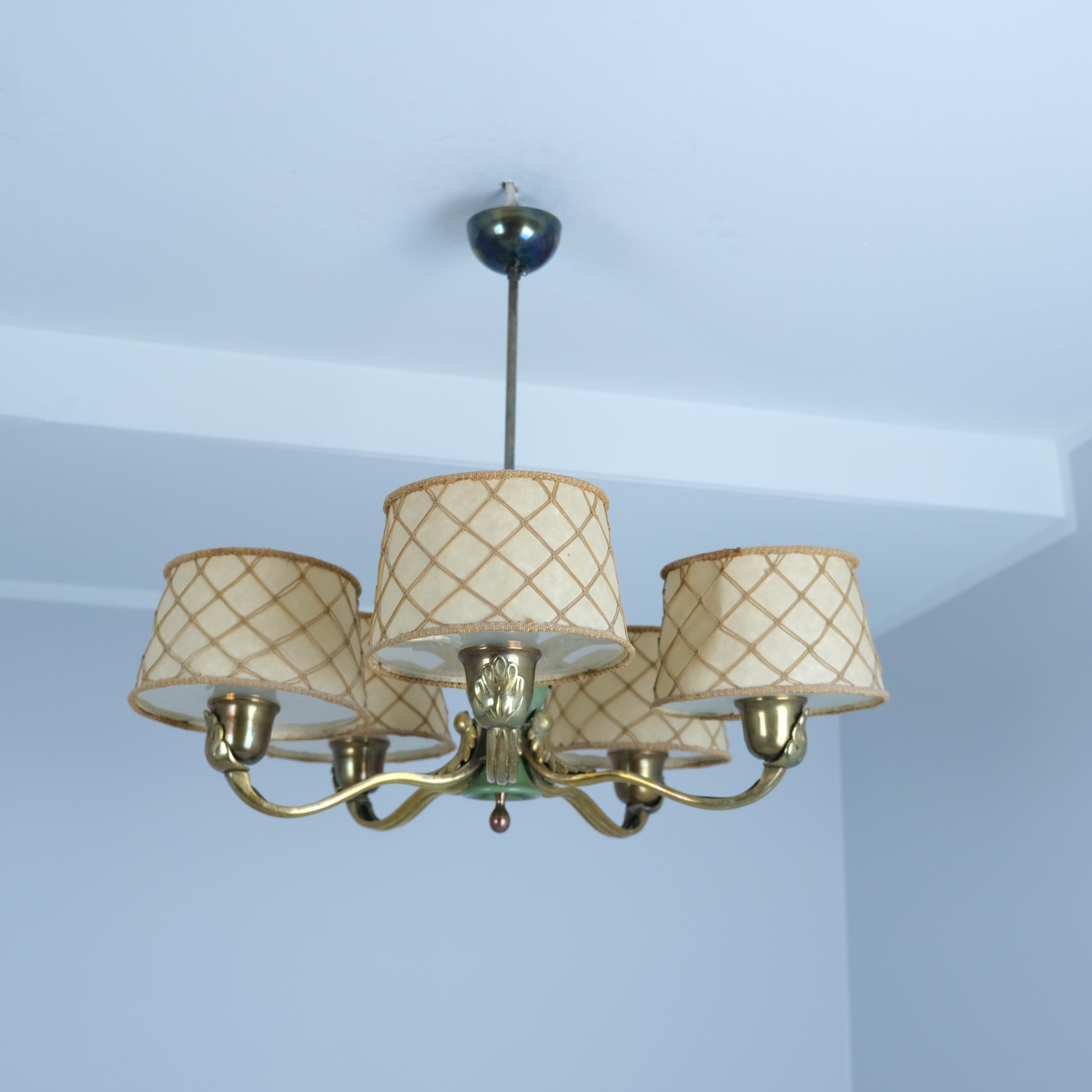 Early and rare model 51057 chandelier designed by Gunnel Nyman for Idman in the 1940s. This striking piece features five classically decorated cast brass arms pertruding from a green painted wooden center. The shades are paper shades with string