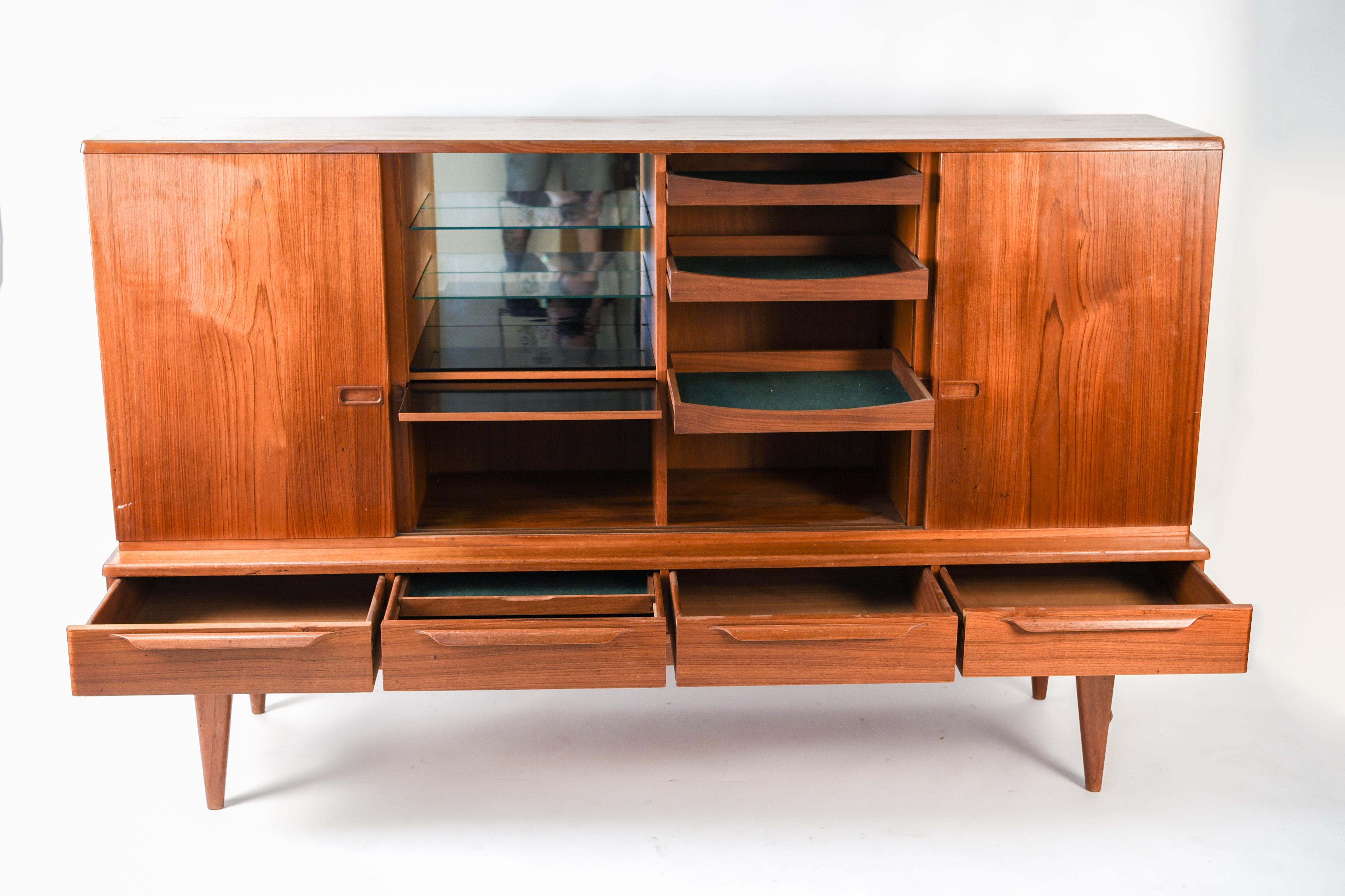 This Danish midcentury teak highboard was designed by Gunni Omann for Omann Jun Mobelfabrik, circa 1960s. This cabinet or sideboard features four sliding doors above four drawers, making for plenty of available storage space.