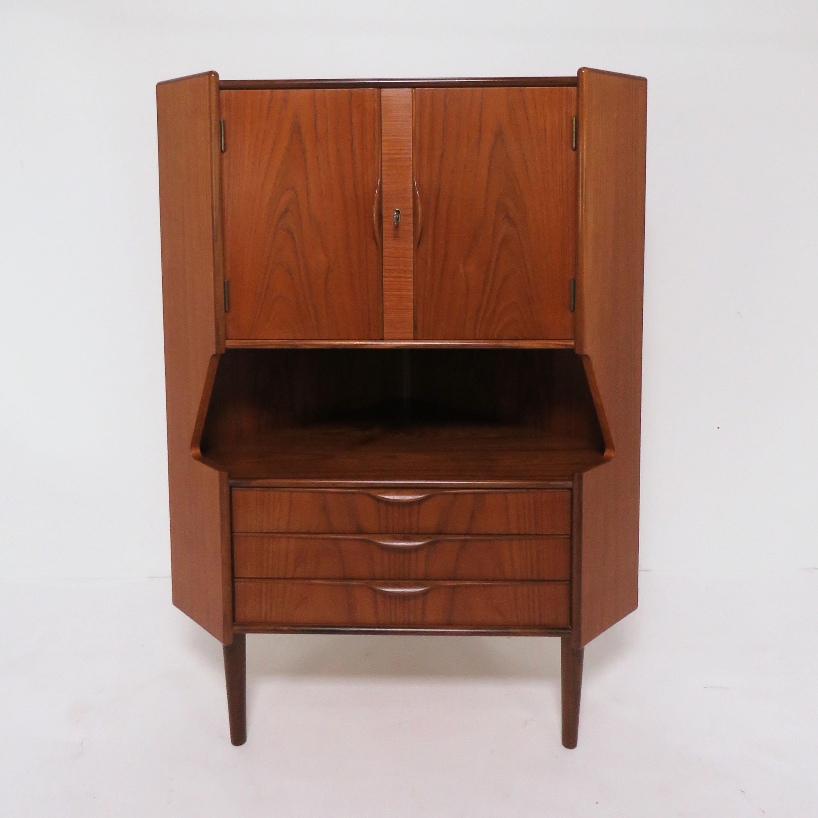 Teak corner cabinet designed by Gunni Omann for Omann Jun, Denmark, circa 1960s. Features three drawers and an open serving space, two doors above (with key) offer storage for barware.

Measures 48.25