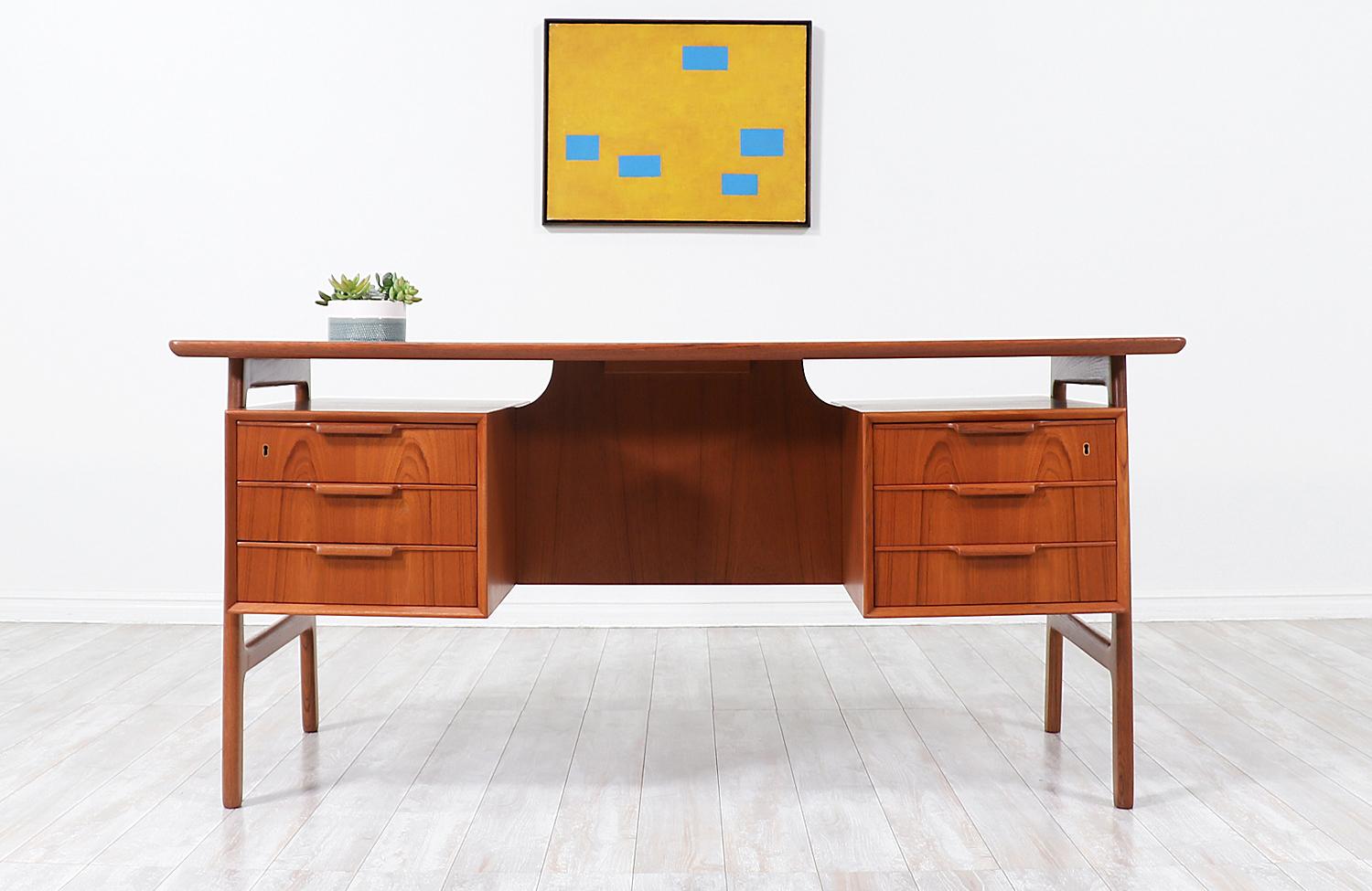 A stunning modern executive desk designed by architect Gunni Omann for his family-owned company Omann Jun, in Denmark, circa 1960s. The handcrafted profile and sculptural Model-75 desk features a sturdy frame that helps elevates the case of drawers