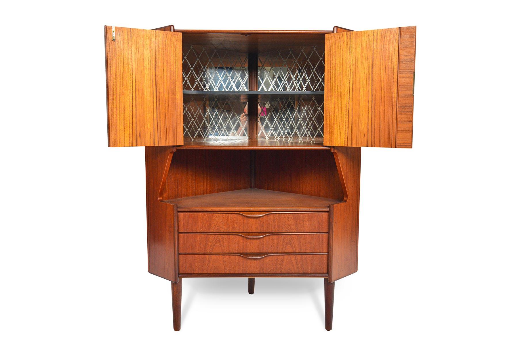 This fabulous Danish modern midcentury corner bar in teak will brighten up any modern home. Designed by Gunni Omann for Omann Jun Møbelfabrik in the 1960s, this sharp piece features two locking cabinet doors which open to an etched, mirror backed