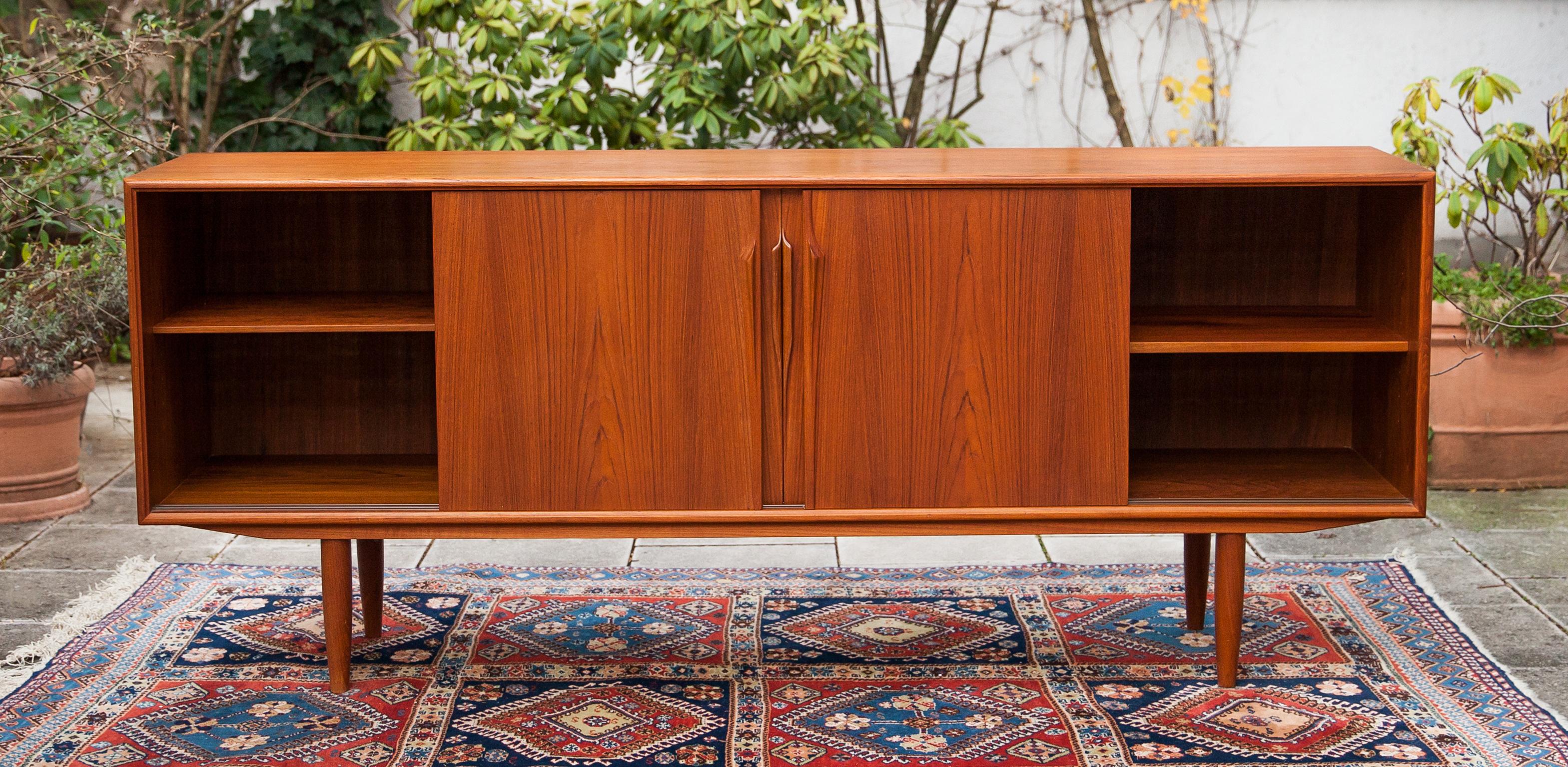 Wonderful midcentury teak sideboard designed by Gunni Omann for Omann Jun Mobelfabrik. The bevel-edged case sits on tapered legs and features four sliding doors with long organic handles. Inside are two adjustable shelves and, three tray drawers.