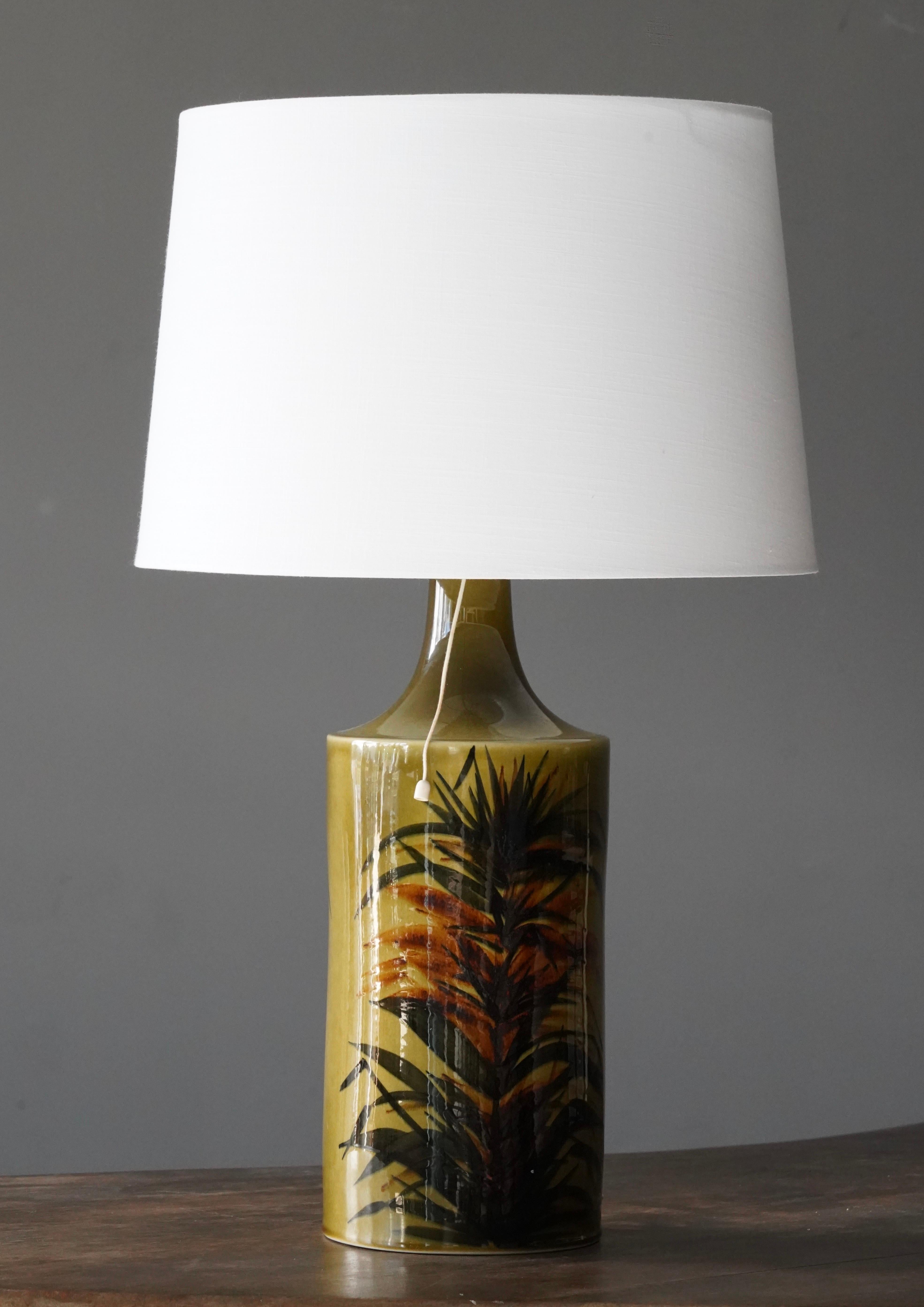 A table lamp, designed by Gunvor Olin-Grönquist. Produced by Arabia, c. 1950s-1960s.

Features glazed stoneware with hand-painted floral motifs.

Dimensions listed are without shade. 
Dimensions with shade: height is 24 inches, width is 15