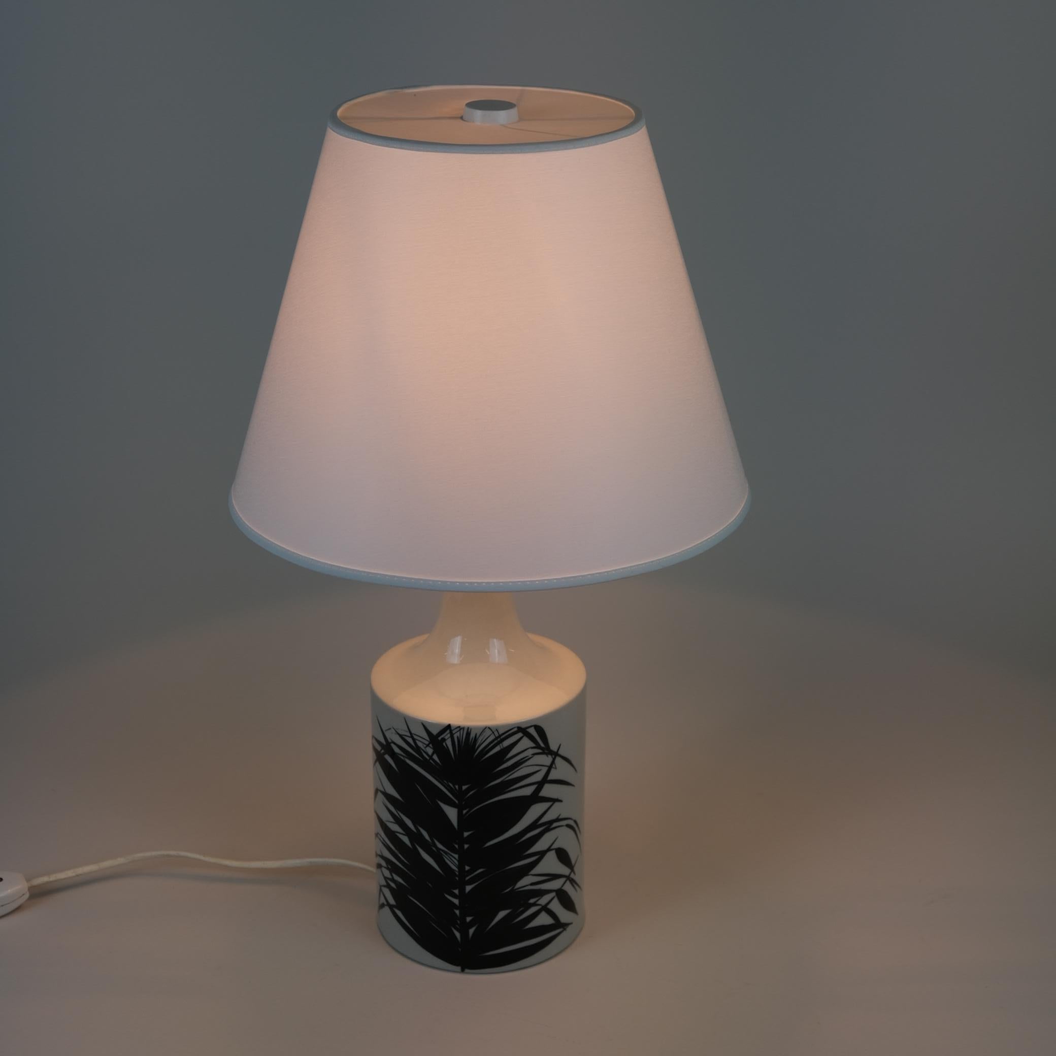 Une belle lampe de table en céramique conçue par Gunvor Design/One en Arabie et pour le célèbre département Stockmann dans les années 1960. La lampe présente de magnifiques feuilles de palmier peintes à la main en bleu sur un fond blanc naturel. La