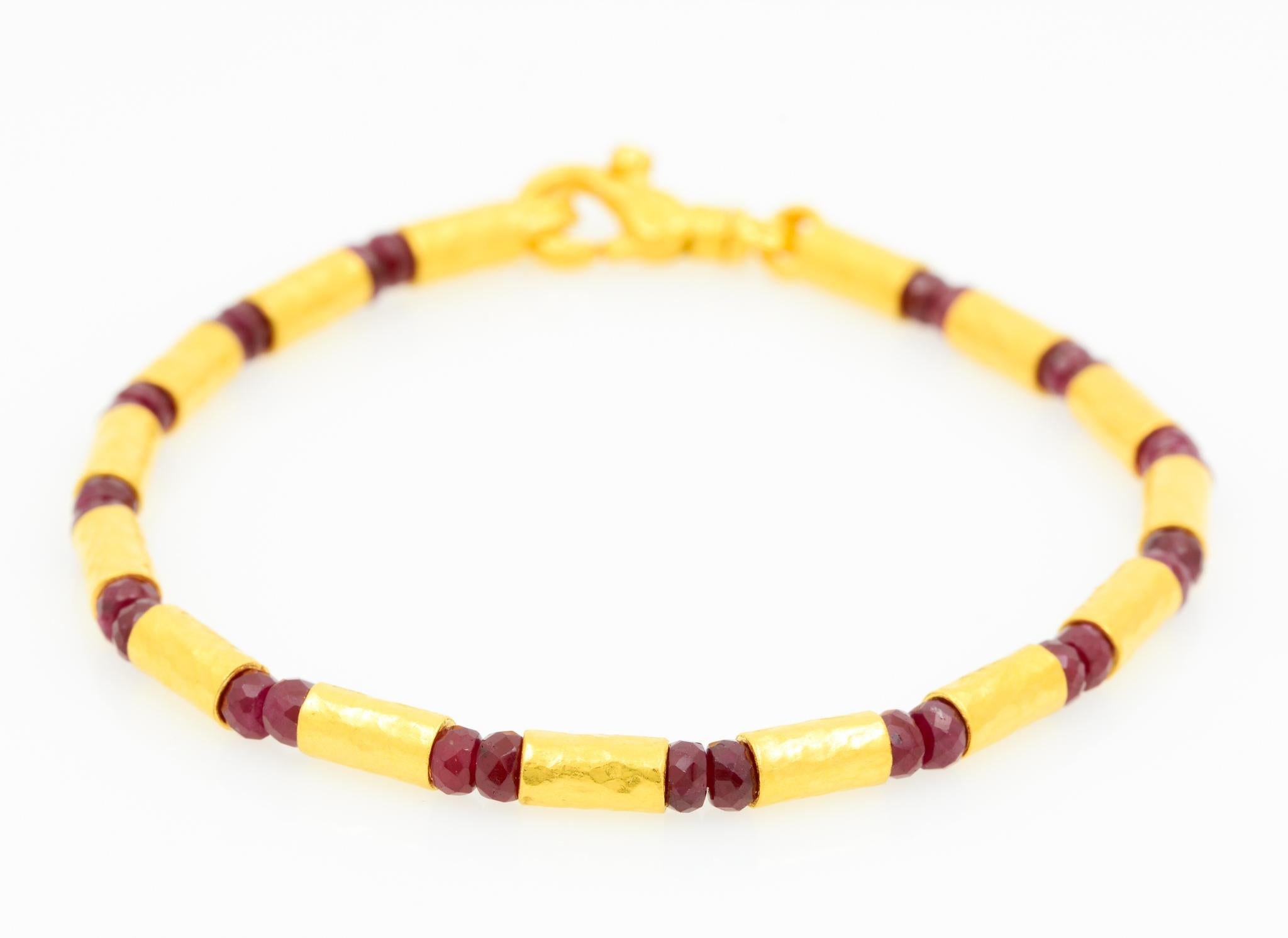 Made by Gurhan, this 24 karat yellow gold beaded bracelet features 15 hammered gold cylinder beads alternating with 28 round faceted ruby beads weighing approximately 9.90 carats combined. The bracelet is 7.5 inches long and has a lobster claw clasp.