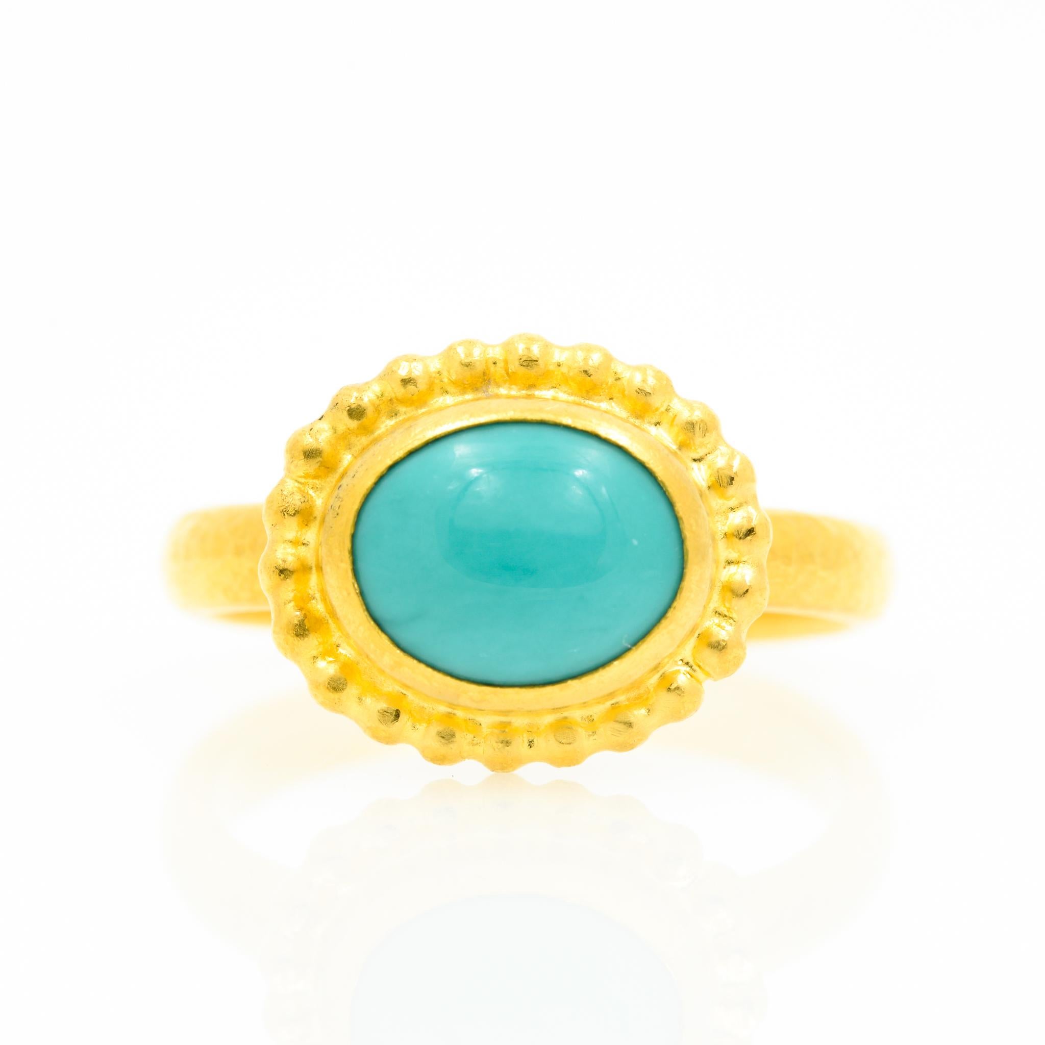 Made by Gurhan, this 24 karat yellow gold ring features a bezel set oval cabochon turquoise with a granulated border. The ring is a size 6.5.