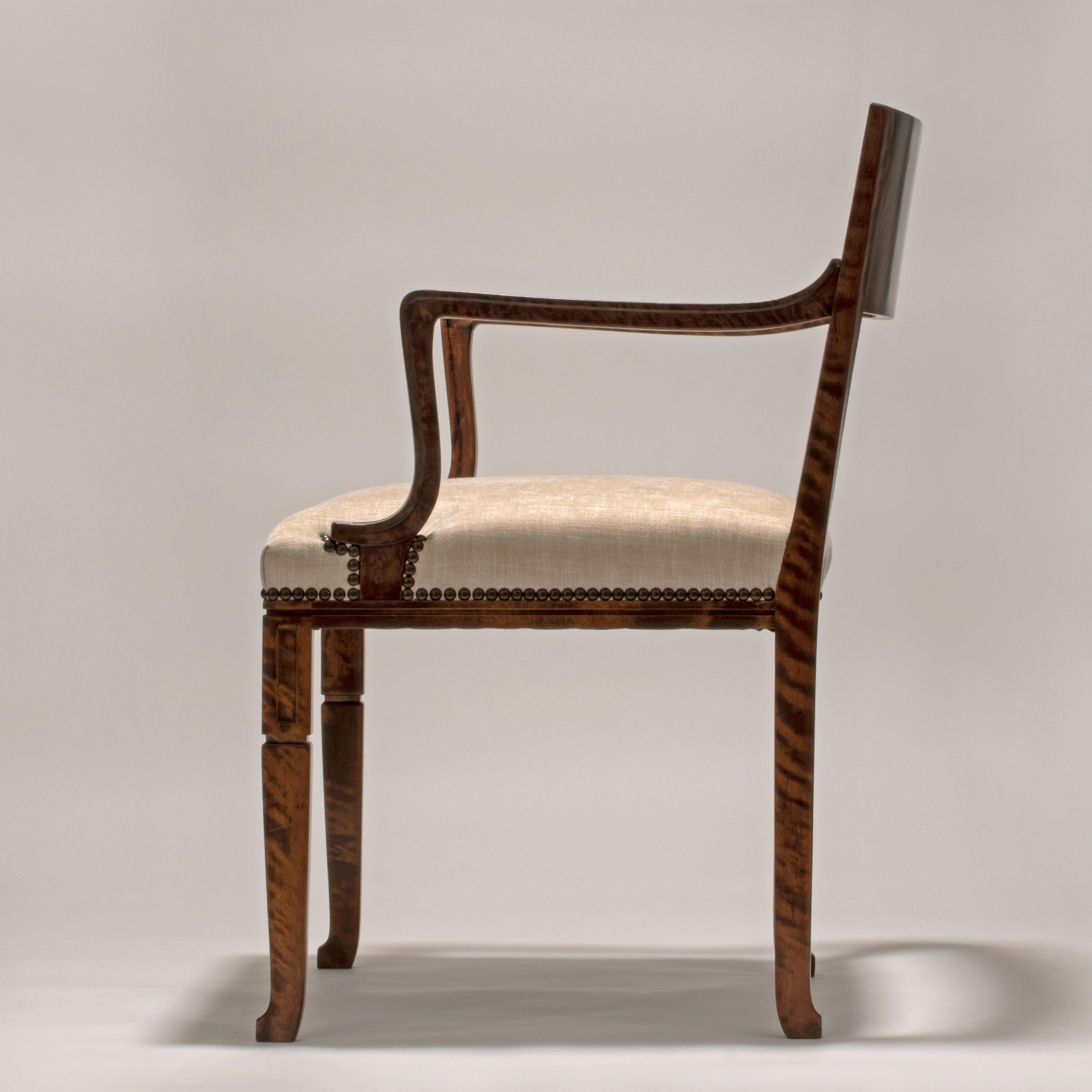 The concave back centering a parquetry panel, issuing two sweeping armrests flanking a wide upholstered seat, above a fluted apron on rectangular legs, the front two legs surmounted by block capitals, terminating in stylized paw feet. Manufactured