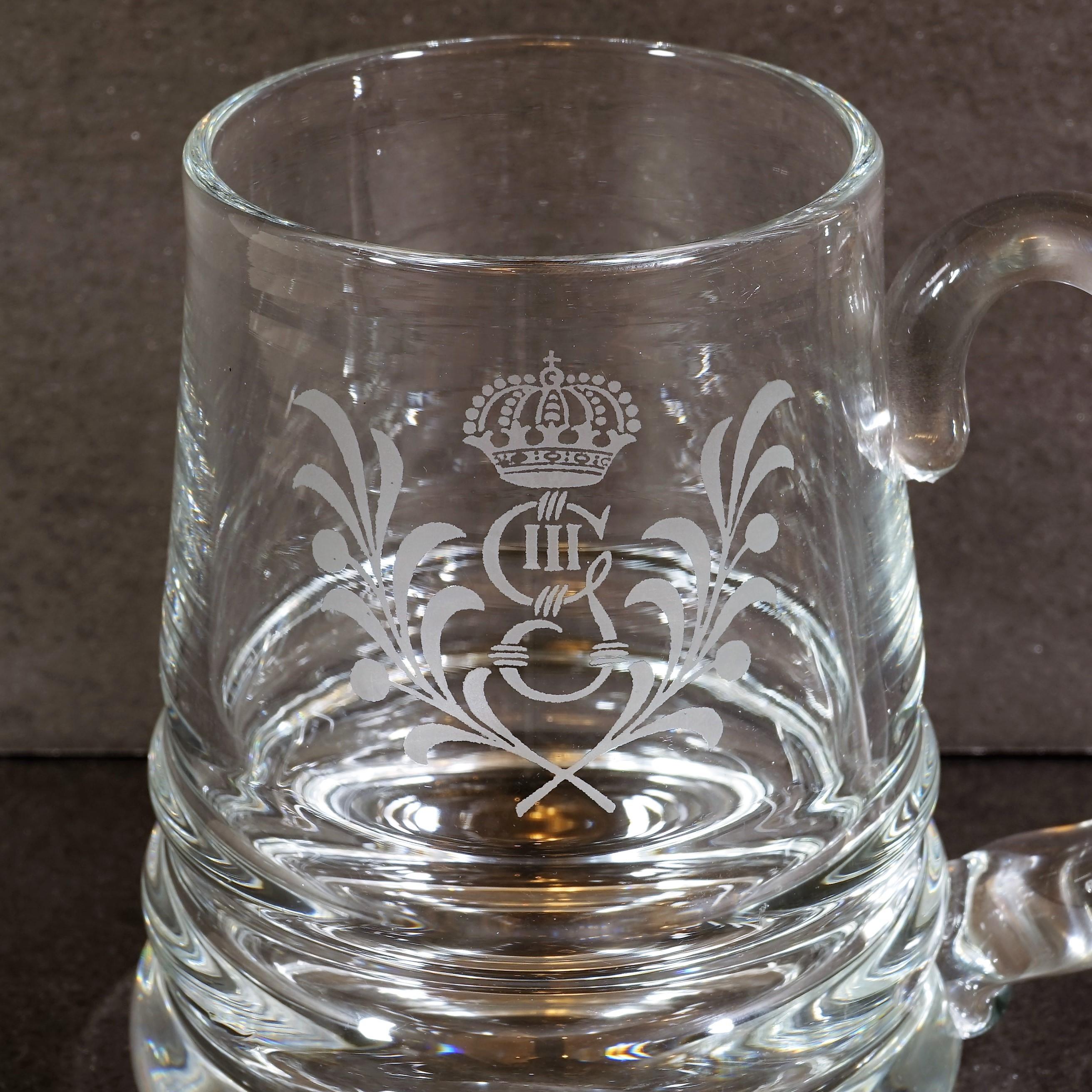 This set of six beer glasses from the Swedish grace period are dedicated to the memory of Gustav III, who was assassinated at a masquerade ball in Stockholm in 1792. They are clear glass vessels, with an acid etching of the King's heraldry.