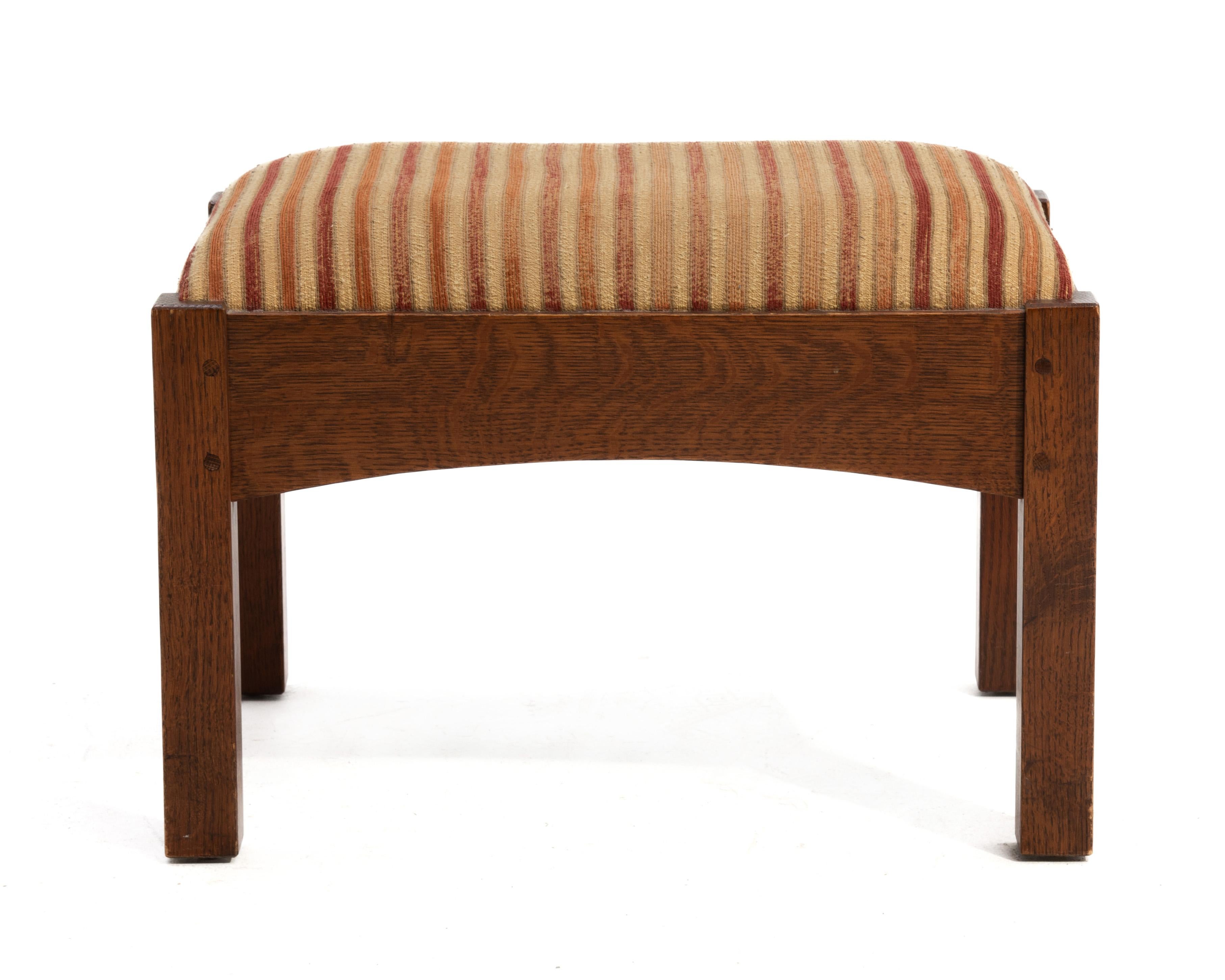 A Gustav Stickley 89-2591 footstool made in 2014. Original finish, quarter sawn oak, arched stretchers, pegged joinery with the original faded fabric. The footstool matches our listing L & J G Stickley Bow Arn Fixed Back Lounge Chair.