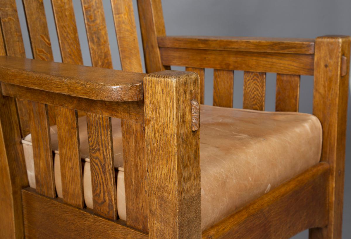 An early 20th century American Mission Arts & Crafts oak framed armchair, made by Harden Co New York circa 1905, attributed to Gustav Stickley, the curved bar and comb back flanked by flattened armrests, the brown leather drop in seat raised on