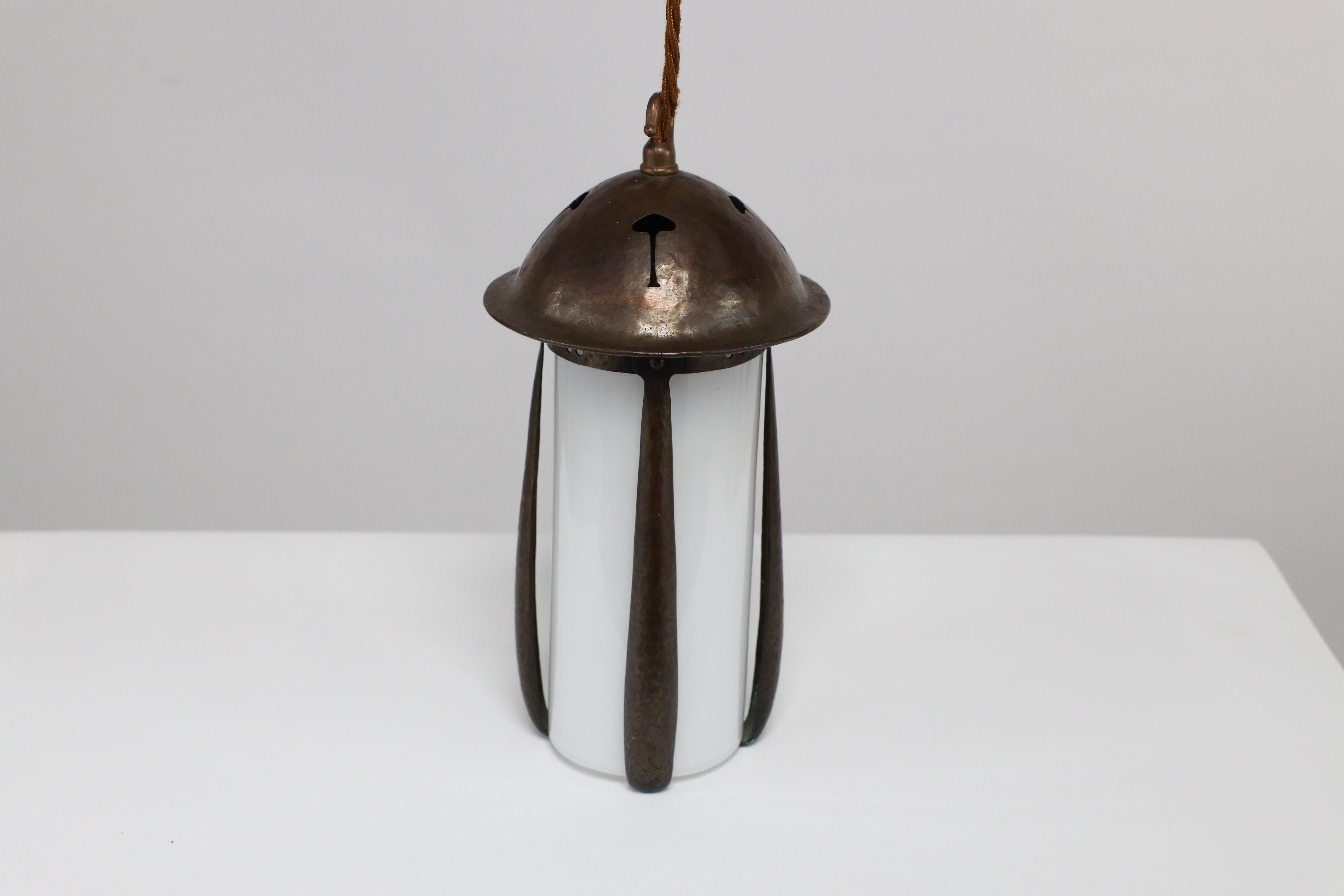 Gustav Stickley in the style of. An Arts and Crafts hand hammered patinated copper lantern with pierced flowers to the hat and pierced split hearts just below the hat, with a milky glass liner that is held in place by the upturns at the bottom of