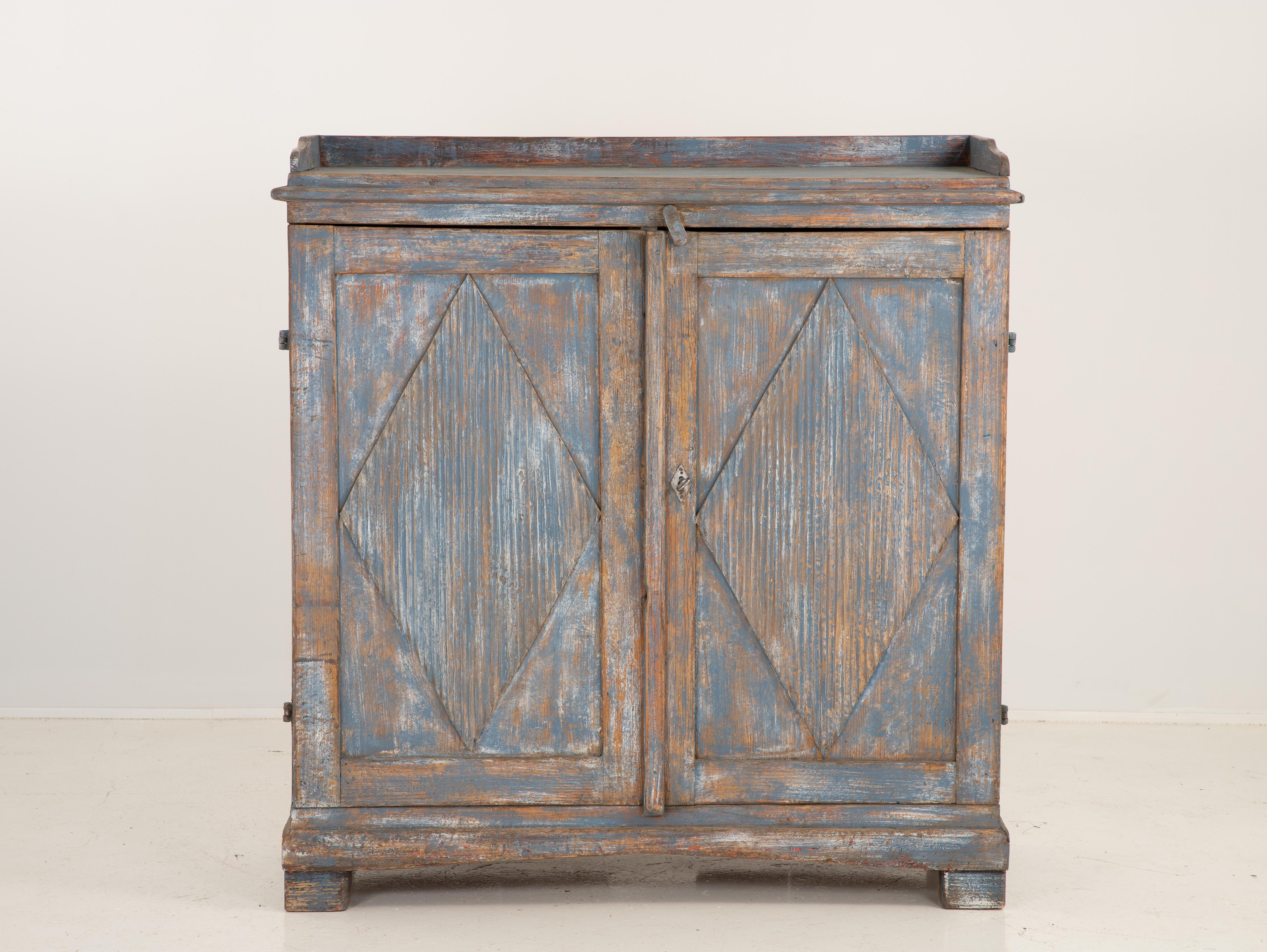 A Gustavian style buffet finished in a rich blue color. Two doors with one shelf inside. Each door has a large reeded lozenge panel, an iconic design typical of the style. The top of the buffet has a gallery edge. Working lock and key.