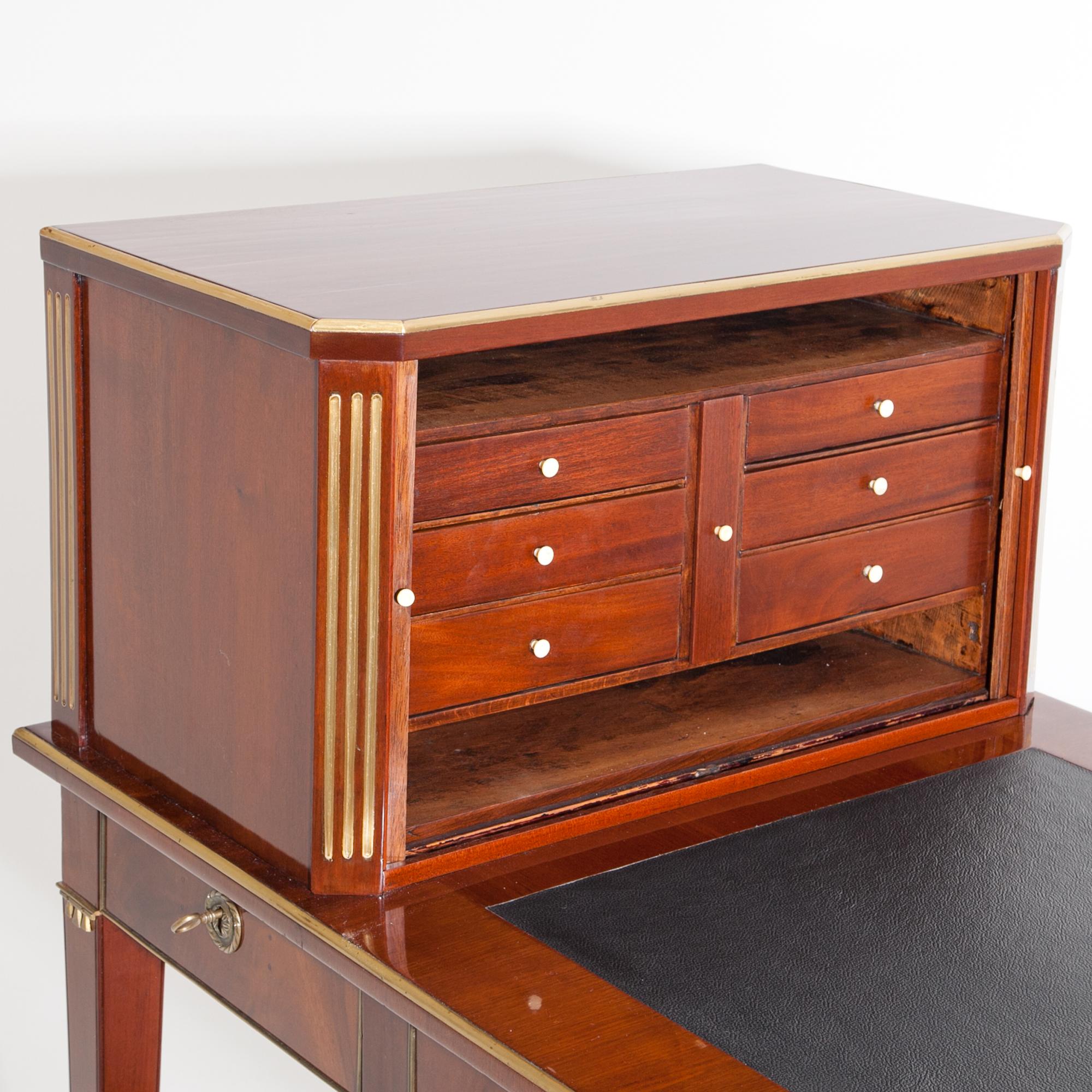 Gustavian desk on tapered legs, veneered in mahogany. The fittings and strips are in brass. The writing surface is covered with a black leather, underneath are three drawers at the front and three corresponding blind drawers on the back. The small