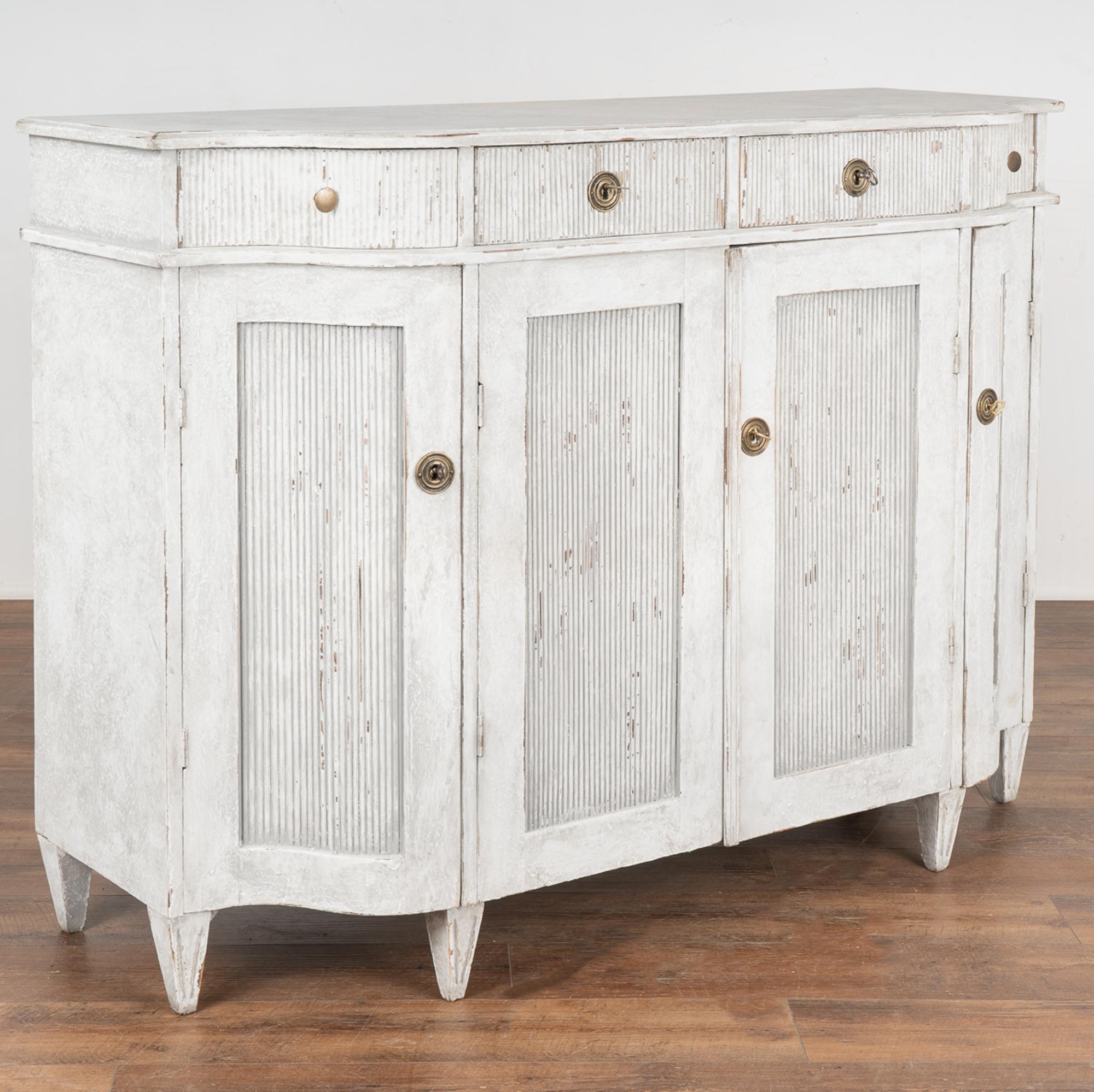 Swedish Gustavian gray painted pine sideboard with attractive curved sides and carved fluted details throughout panel doors and drawers.
It is the curves of the far right and left drawers and doors that create the visual appeal of this lovely