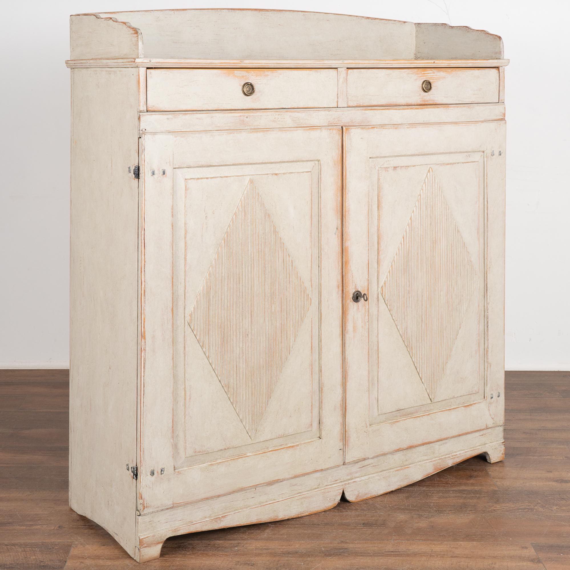Gustavian tall pine sideboard or serving buffet with traditional decorative fluted diamond panels on cabinet doors, two small upper drawers with brass pulls.
One key included to use as pull for doors. 
The soft dove gray exterior is slightly
