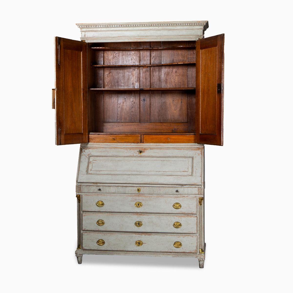 Elegante und architektonische gustavianische Kommode / Sekretär in Eiche mit hellgrauer Farbe. Schreibklappe und Schubladen innen blau lackiert.

Das Bureau / Secrétaire besteht aus zwei Teilen: einem oberen Schrank mit einem profilierten Gesims,