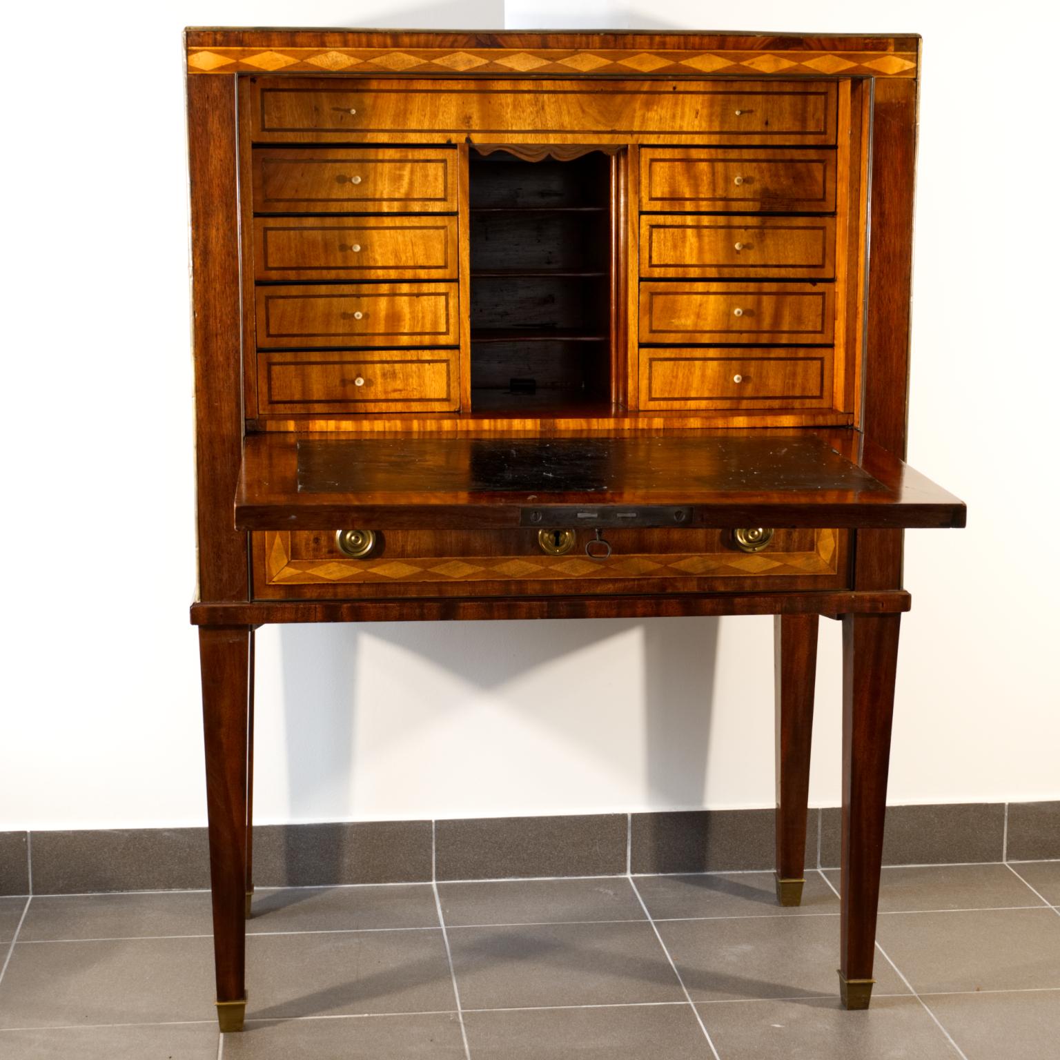 Swedish Gustavian mahogany writing cabinet. The writing part is covered with a black patent leather, with visible traces of use. The inner drawers have bone handles. The upper part is covered with mahogany veneer with brass strips and handles. The