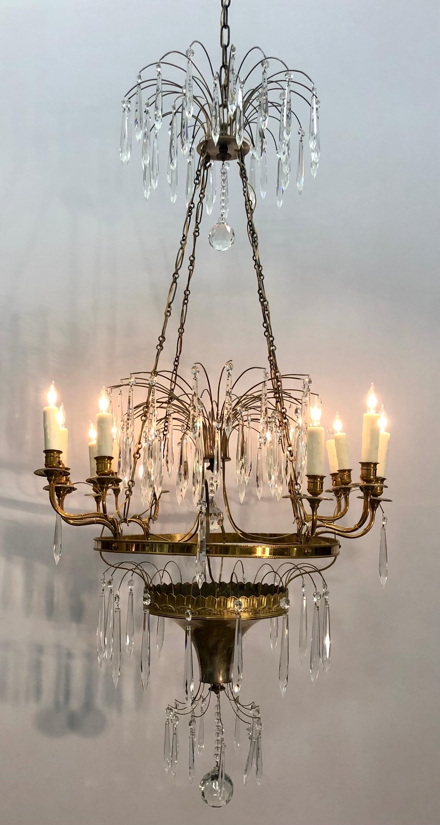 This Regal Gustavian Period Chandelier in the Russian Imperial Style has twelve candle branches and is fashioned in doré bronze, silverplated bronze, and is pinned with faceted icicle crystal pendants. The elegant corona has bronze sprays with