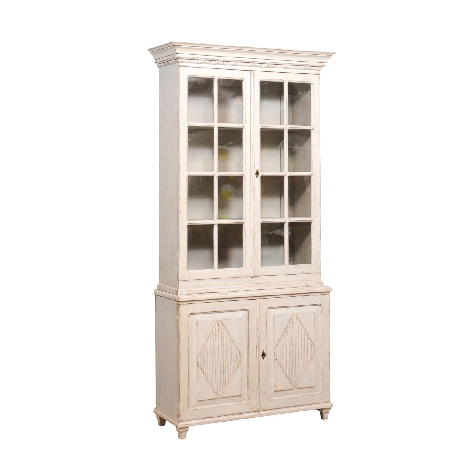 A Swedish Gustavian style painted wood vitrine cabinet from circa 1880 with light gray painted finish, glass doors and carved diamond motifs. This Swedish Gustavian style vitrine cabinet, hailing from the late 19th century, effortlessly marries