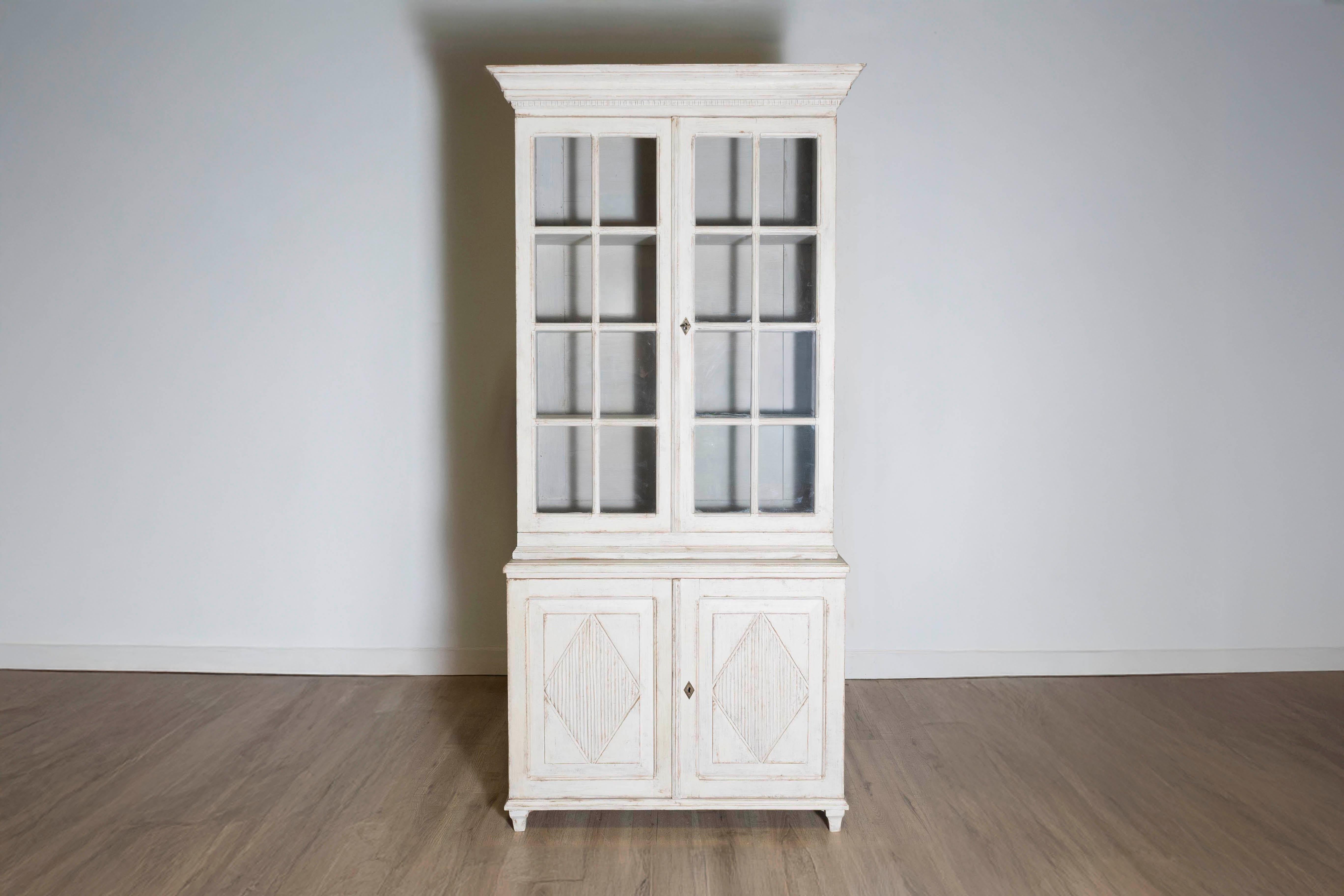 A Swedish Gustavian style painted wood vitrine cabinet from circa 1880 with light gray painted finish, glass doors and carved diamond motifs. This Swedish Gustavian style vitrine cabinet, hailing from the late 19th century, effortlessly marries